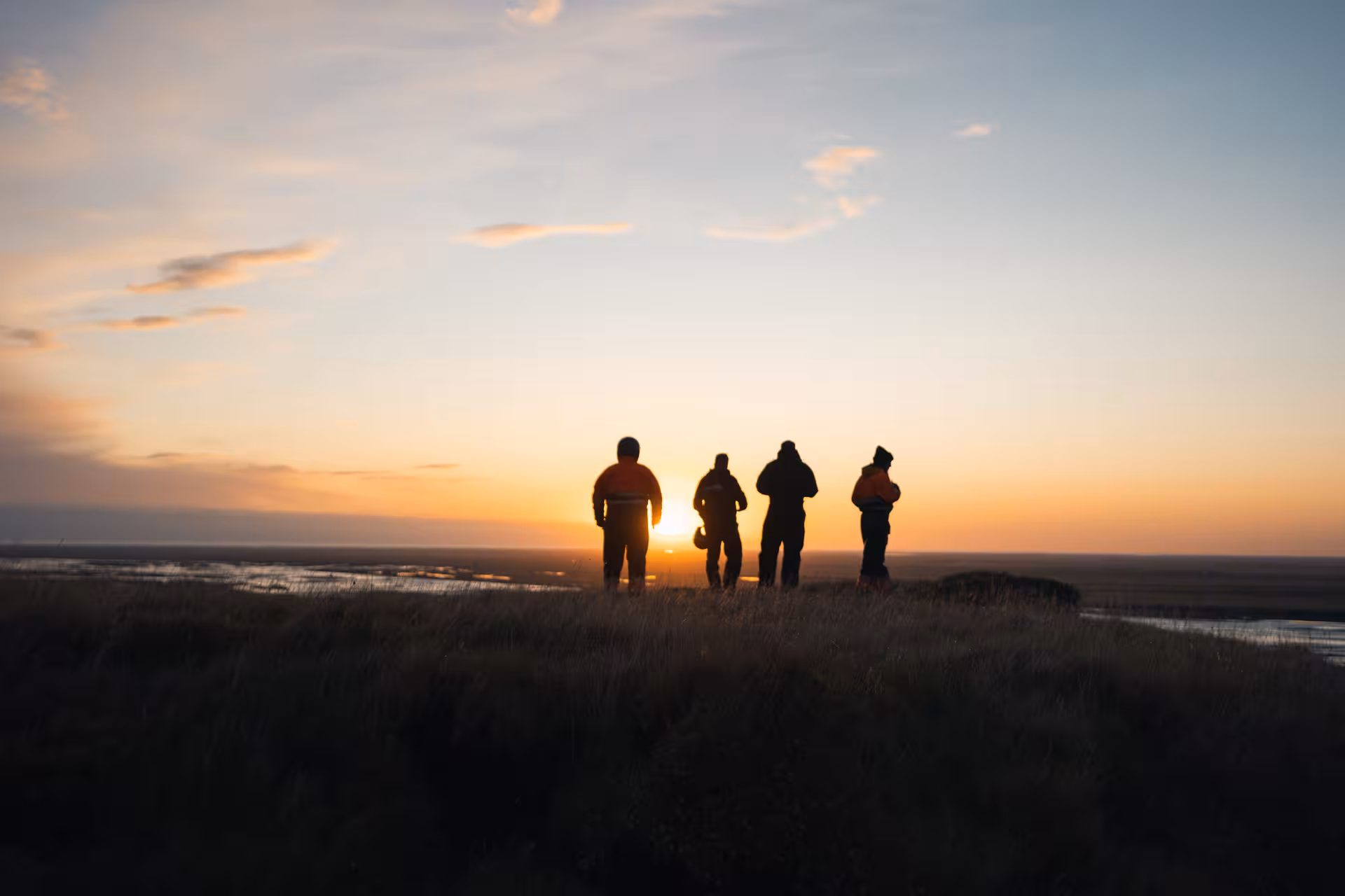Four silhouetted people standing on Iceland tundra watching sunset during off-road ATV buggy tour