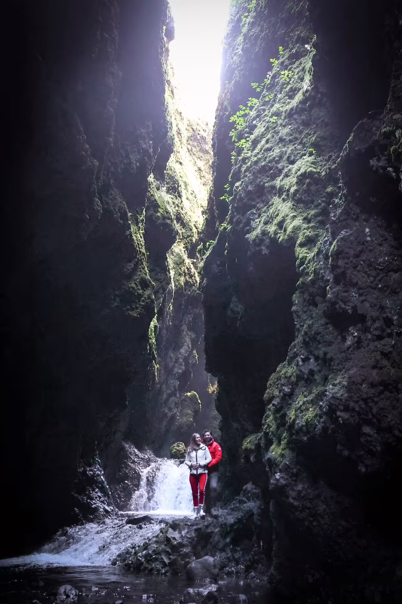 A couple explores a dramatic moss-covered Iceland canyon gorge with hidden waterfall on a South Coast adventure tour