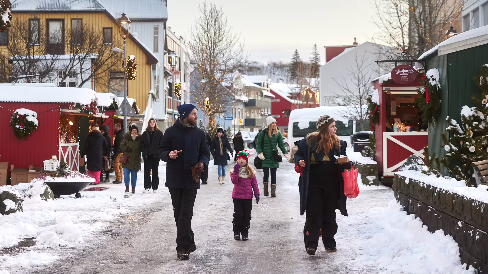 Family walking through a snowy Icelandic Christmas market with festive stalls and holiday decorations
