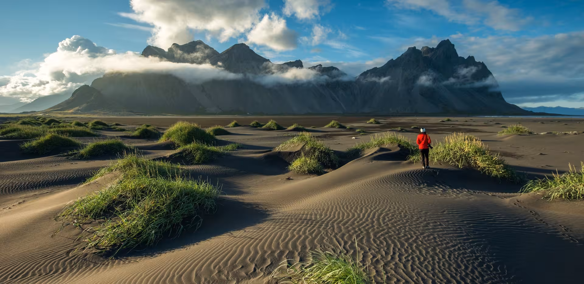 Traveler exploring the picturesque black sand dunes with Vestrahorn mountain in the background on Iceland's self-drive tour.