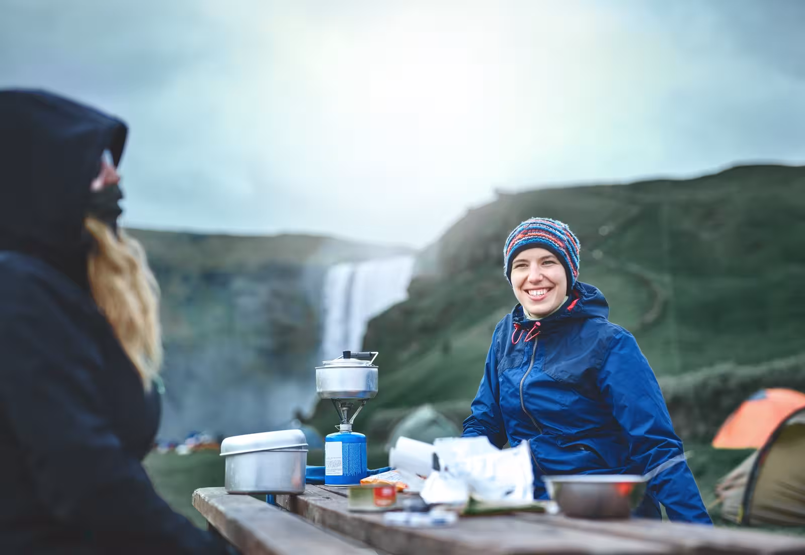 Smiling travelers enjoy a scenic picnic near Skógafoss waterfall, highlighting the adventure of Iceland's self-drive tour.