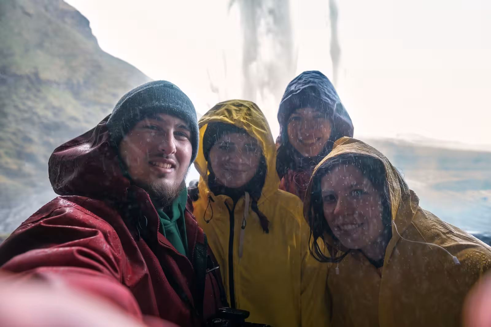 Group of travelers in raincoats taking a selfie behind Seljalandsfoss waterfall during Iceland's complete circle tour.