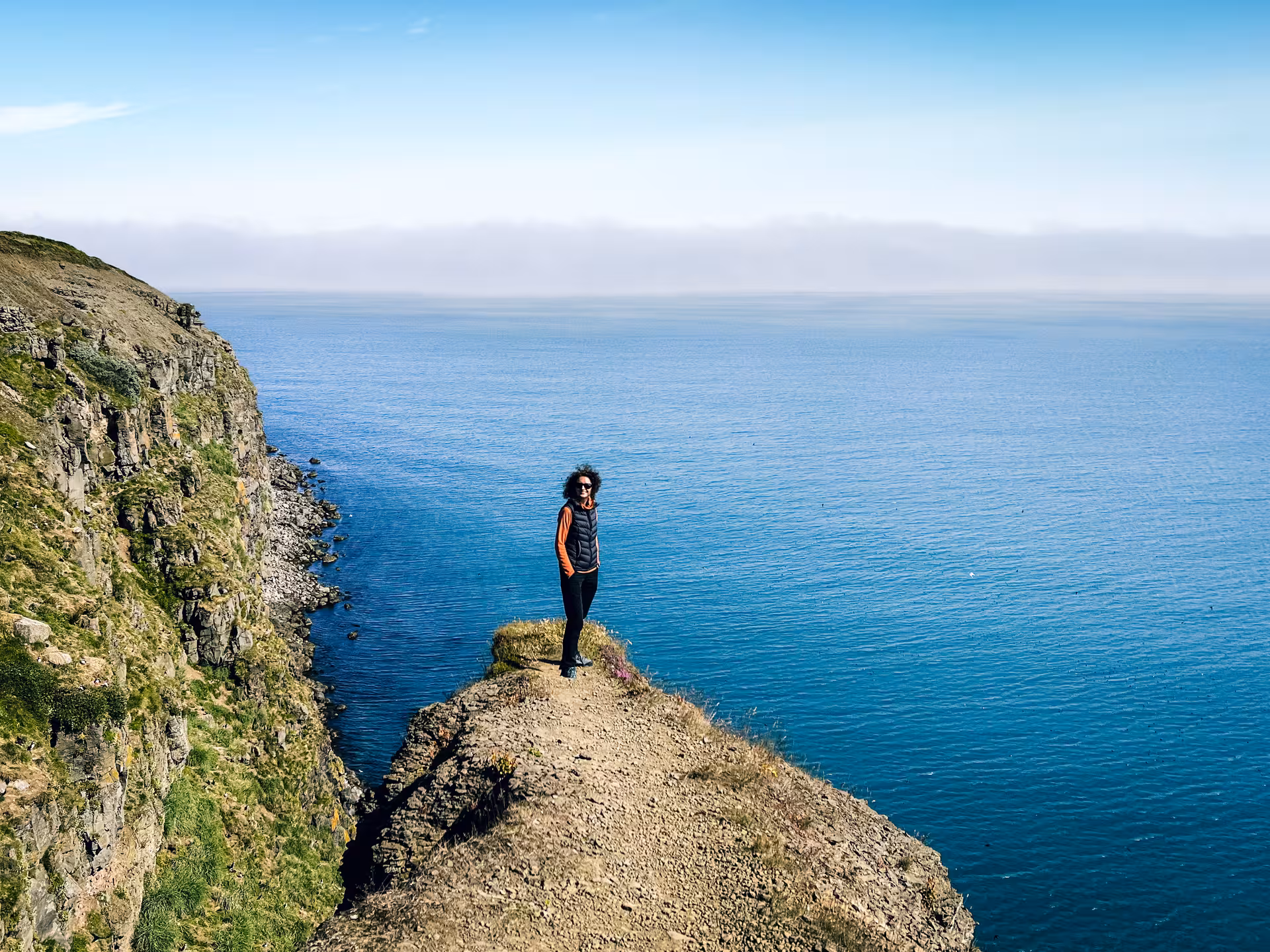 Hiker on dramatic sea cliff viewpoint on Iceland Diamond Circle tour, rugged coastline and blue ocean