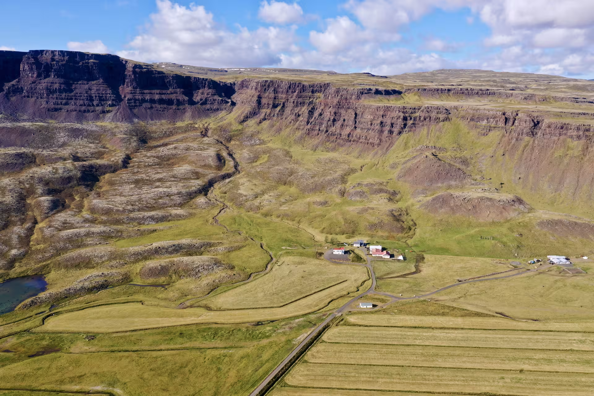 Aerial view of an Icelandic farm nestled beneath dramatic layered cliffs and green valleys on the Golden Circle