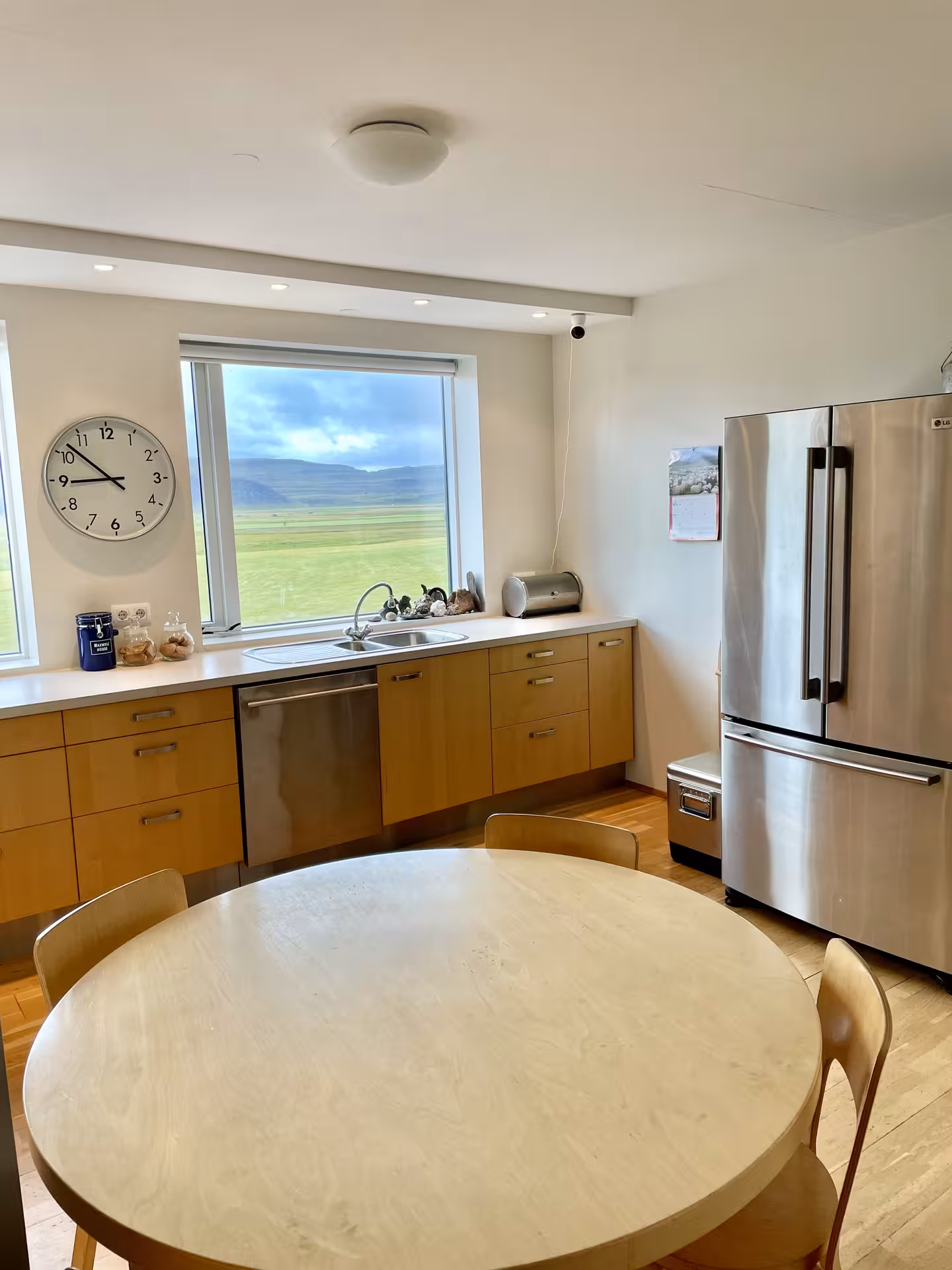 Modern Icelandic farmhouse kitchen with wooden cabinets, round dining table, and scenic green valley view through large window