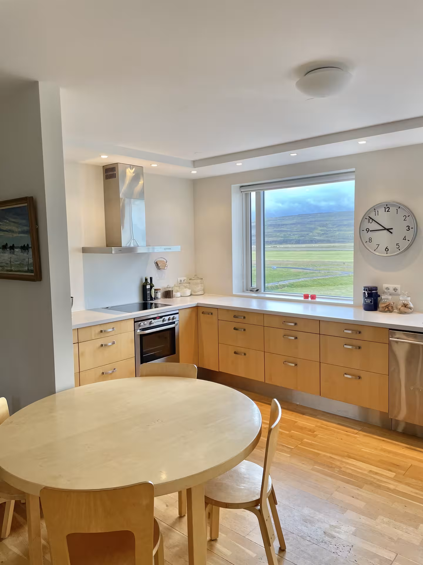Modern farmhouse kitchen with wooden cabinets, round dining table, and panoramic view of Icelandic green fields