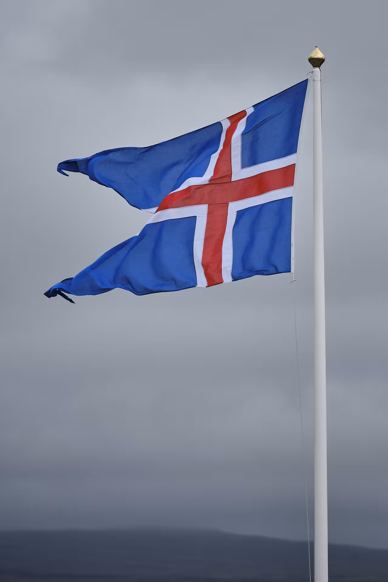 Iceland flag waving on a white flagpole against a cloudy grey sky