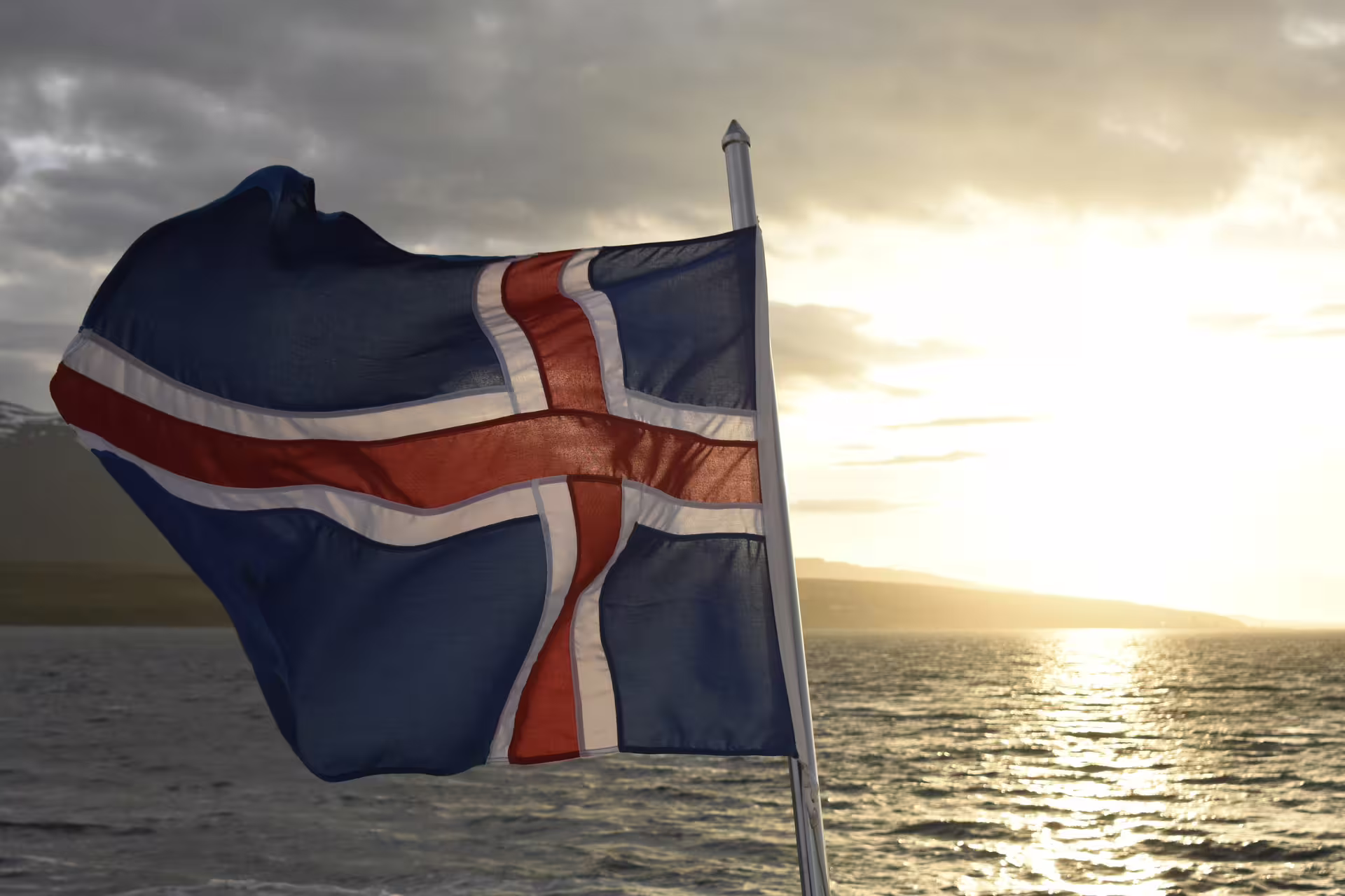 Icelandic flag waving over calm ocean waters at sunset near Akureyri