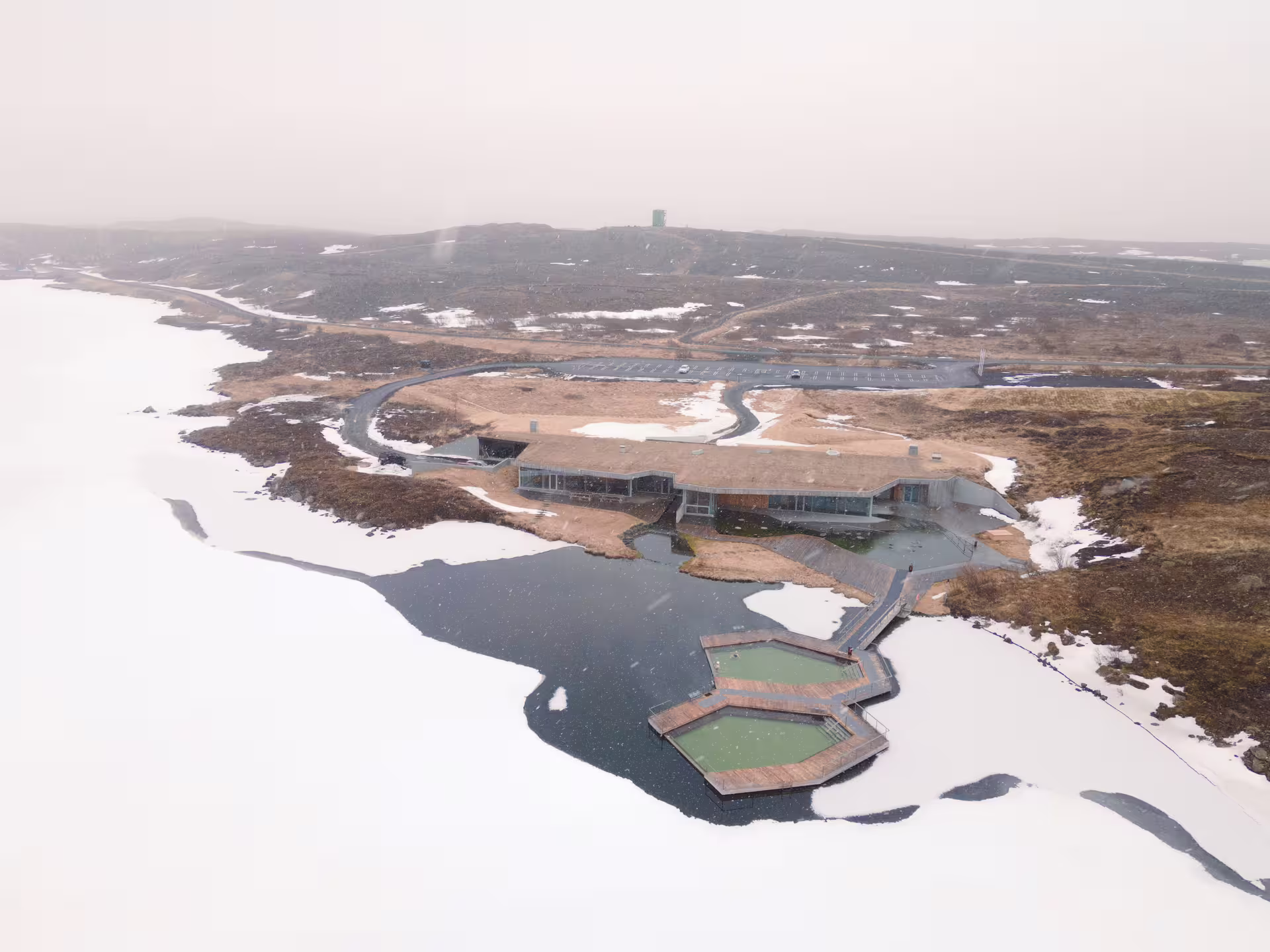 Aerial view of geothermal hot spring baths beside a frozen lake in Iceland winter landscape