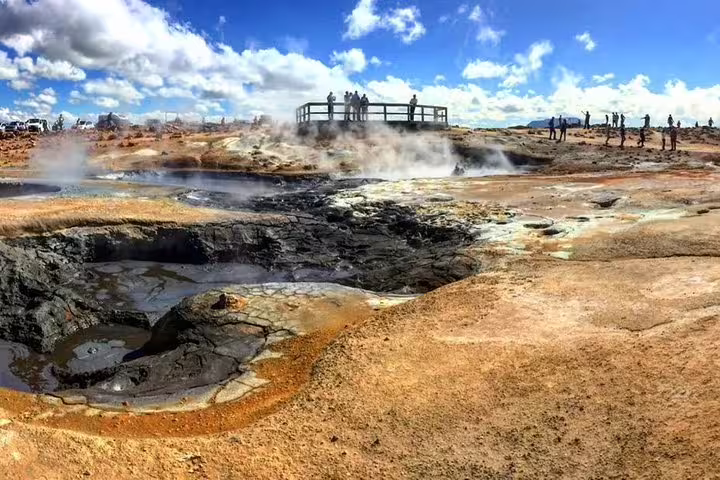 Steaming geothermal hot springs with colorful mineral deposits and tourists on viewing platform in Iceland