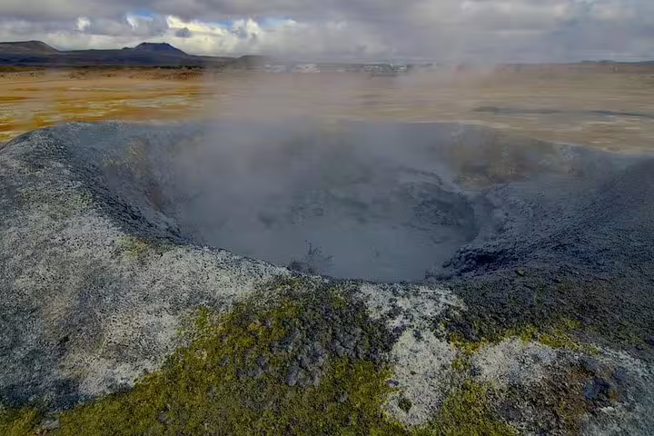 Steaming geothermal mud pool surrounded by moss-covered volcanic rock in Iceland's highland landscape