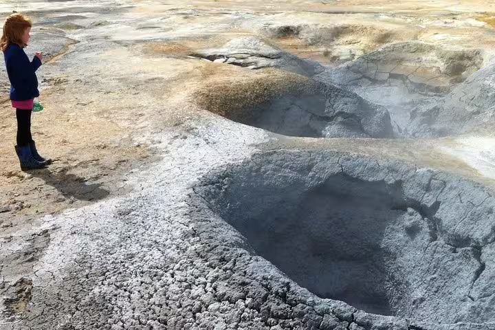 Child standing near steaming geothermal mud pools in Iceland's volcanic landscape