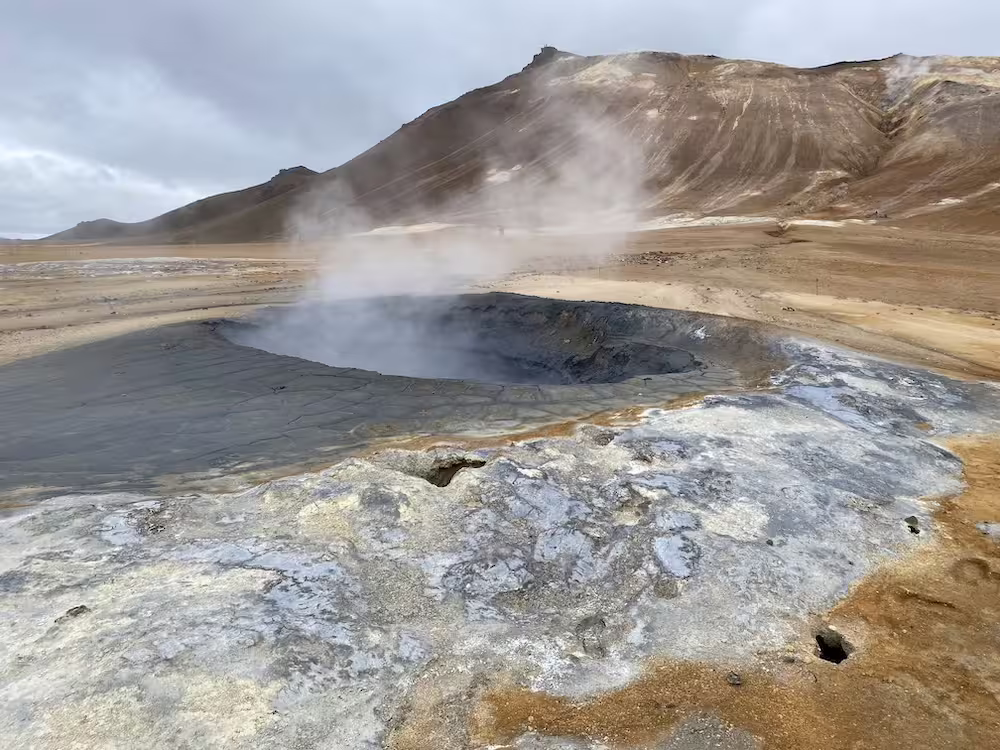 Steaming geothermal mud pools with volcanic mountain backdrop in Iceland