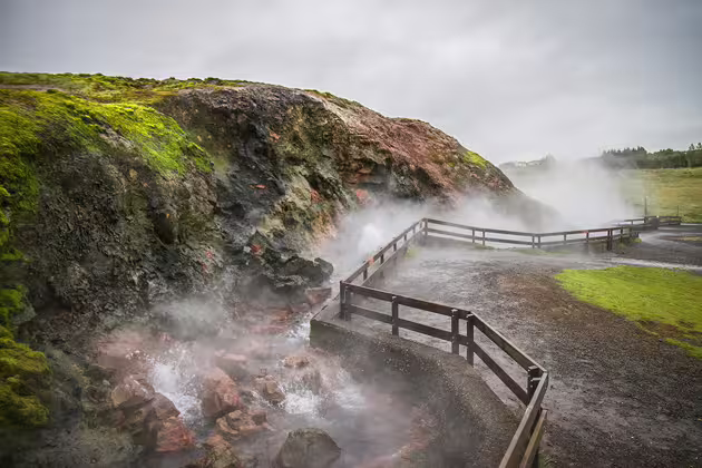 Steaming geothermal hot spring with wooden walkway and moss-covered lava rocks in Iceland