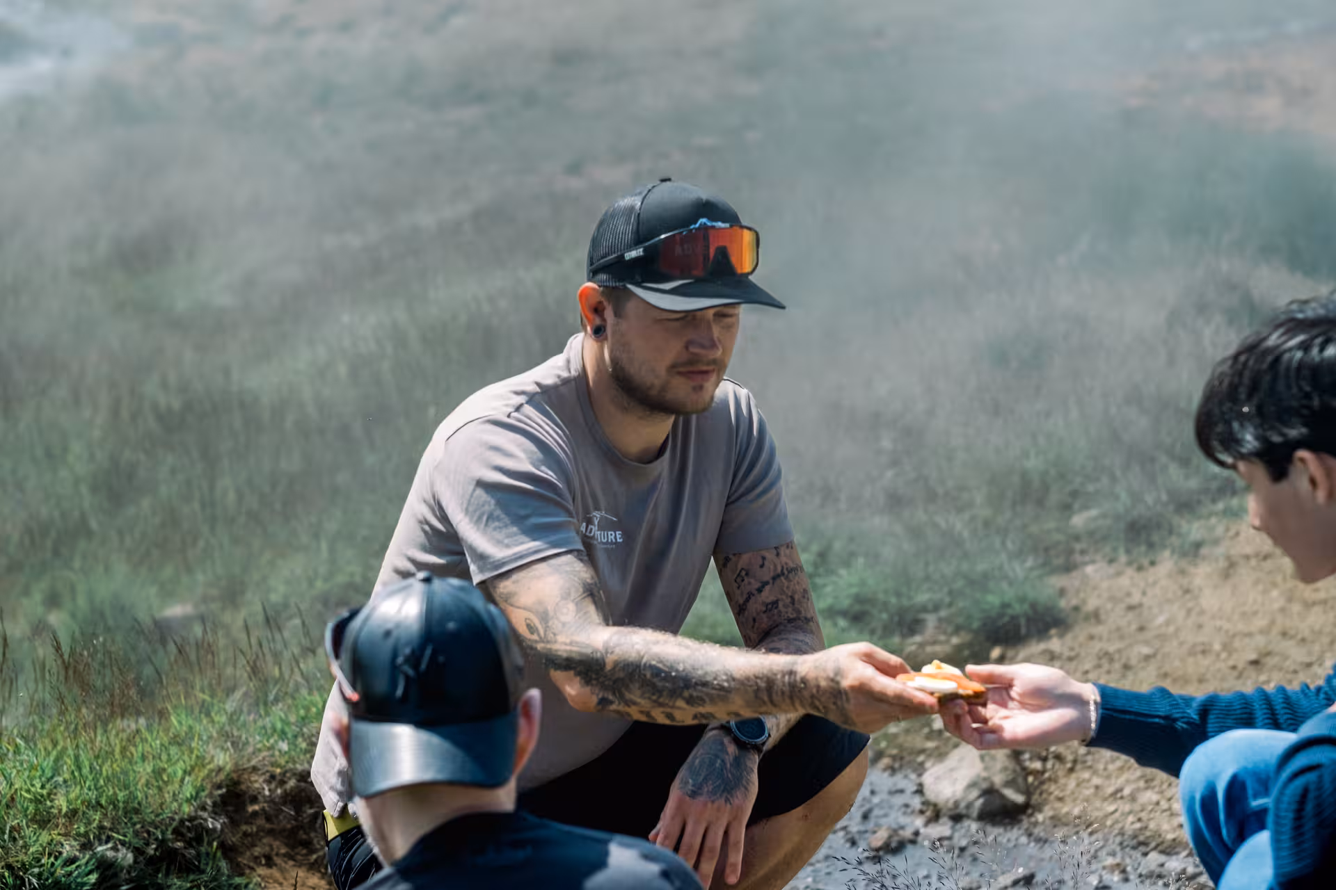Tattooed guide sharing food with hikers during a rest stop in Iceland's geothermal valley near Hengill Volcano