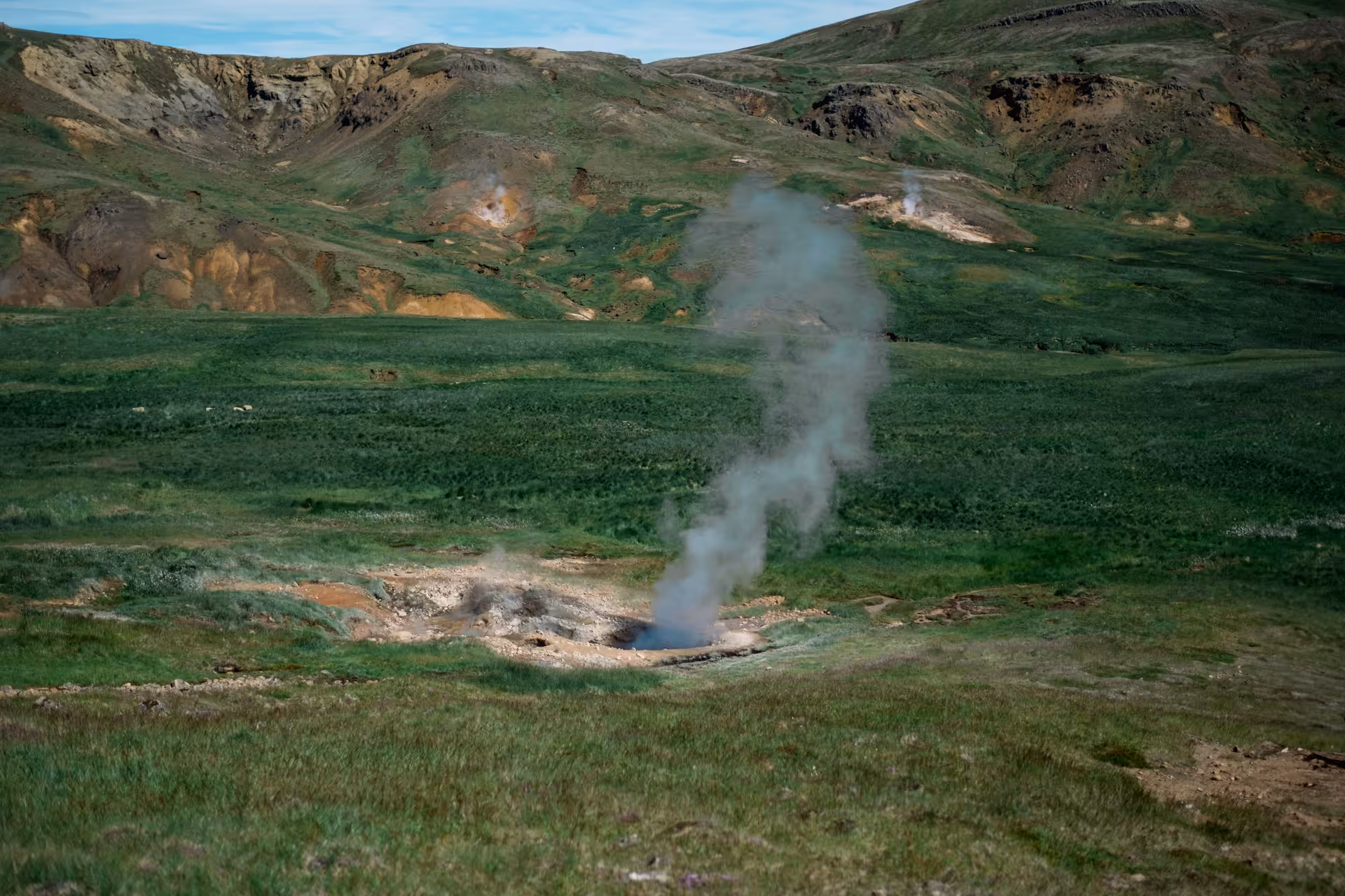 Geothermal steam vent rising from green valley near Hengill Volcano, Iceland