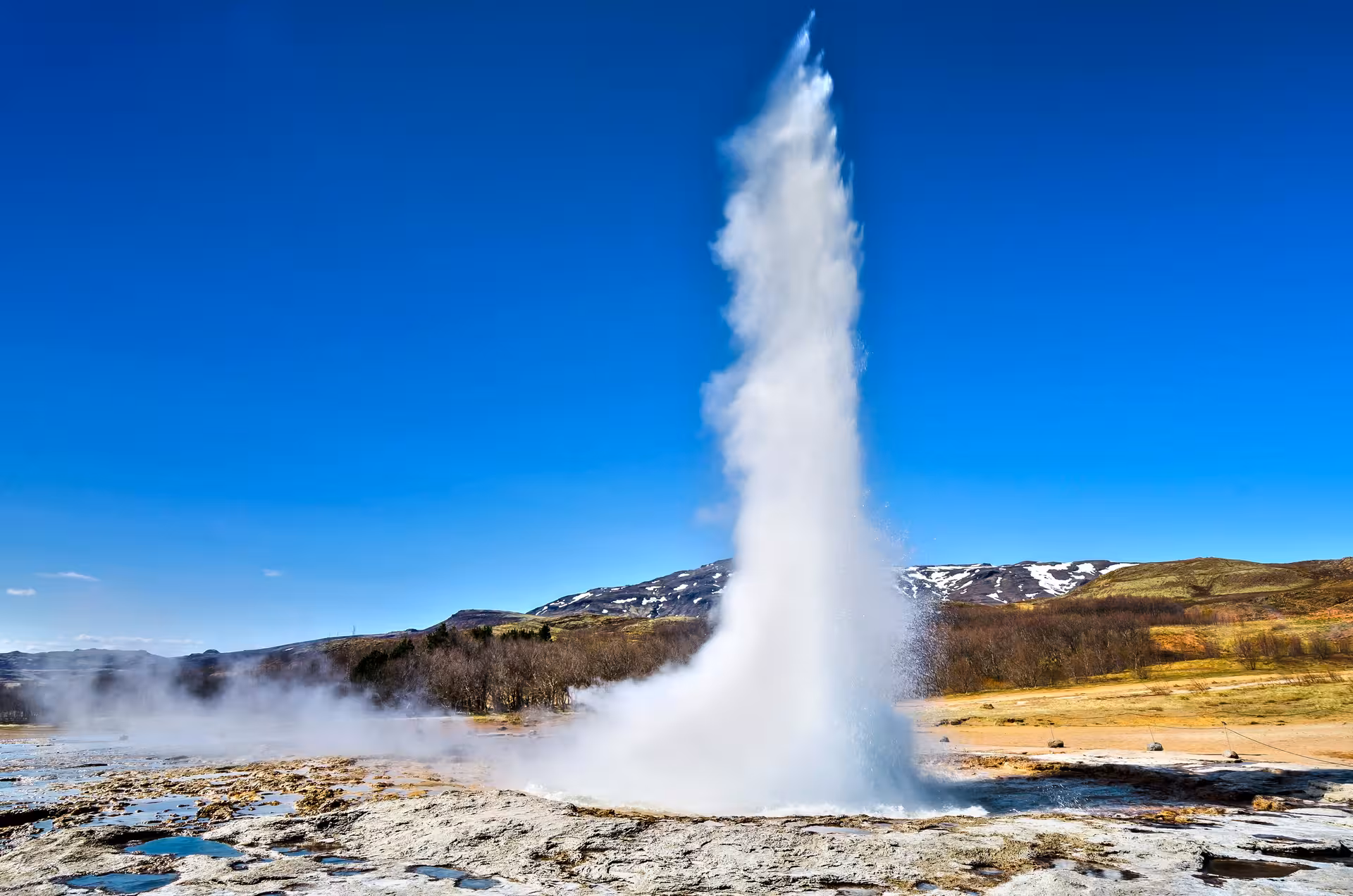 Powerful geyser eruption under a clear blue sky, a highlight of Iceland's 3-Day Northern Lights Tour.