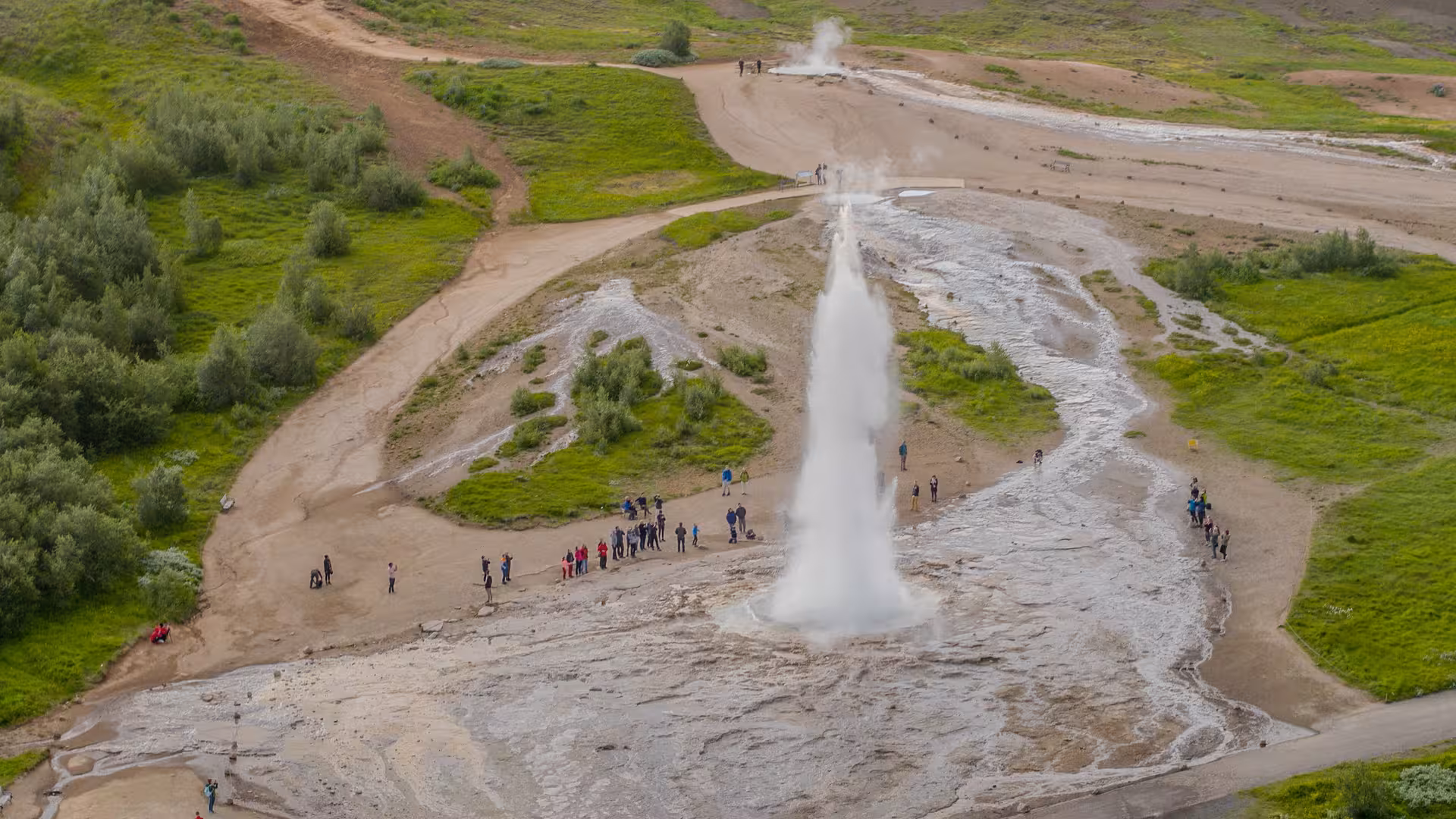 Tourists gather around a powerful geyser eruption in Iceland, highlighting natural wonders on the South tour.