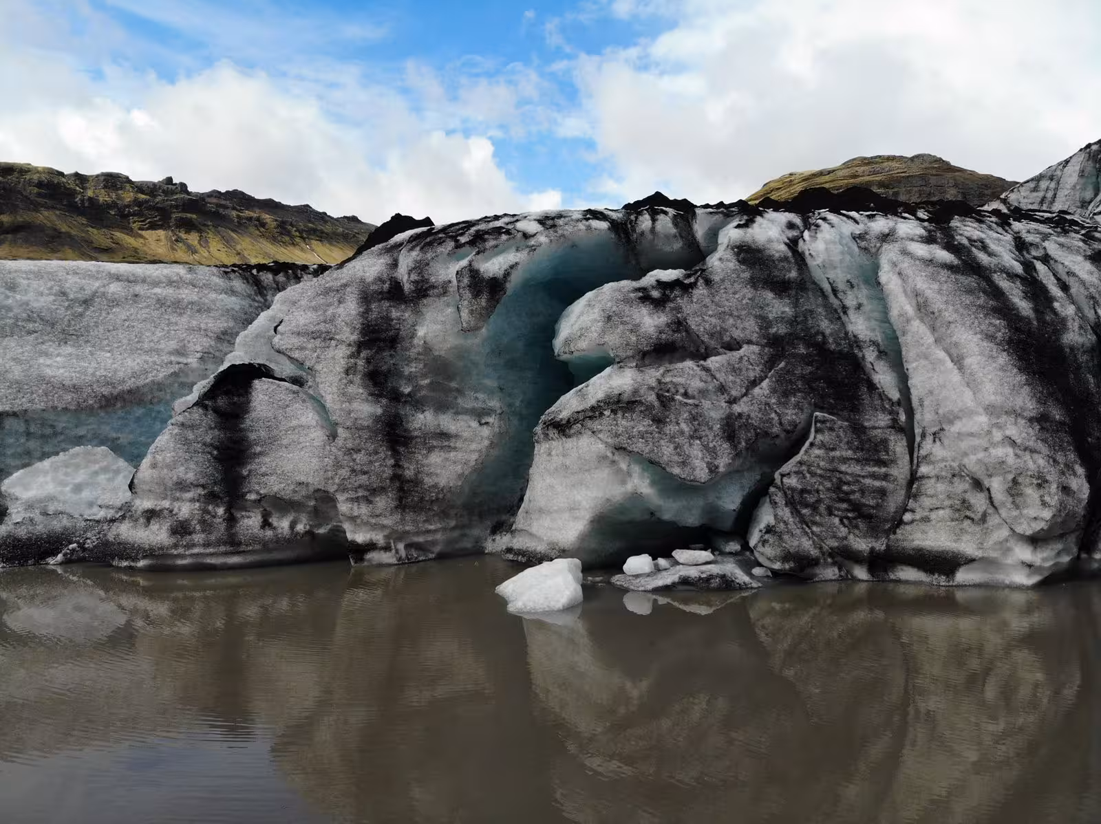 Stunning volcanic ash-streaked glacier cave reflected in glacial lagoon on South Coast Iceland private day trip from Reykjavik