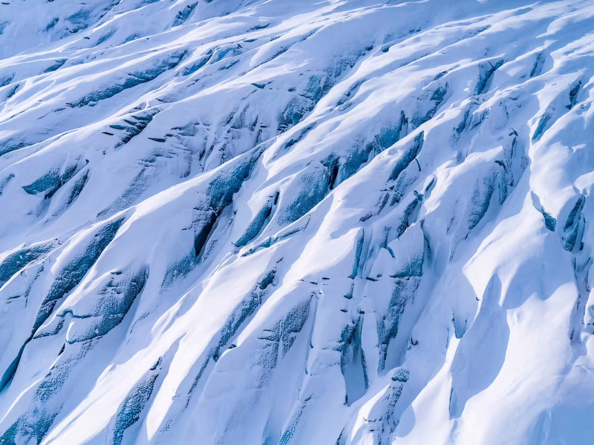 Snow-covered glacier crevasses with blue ice visible from aerial view in Iceland