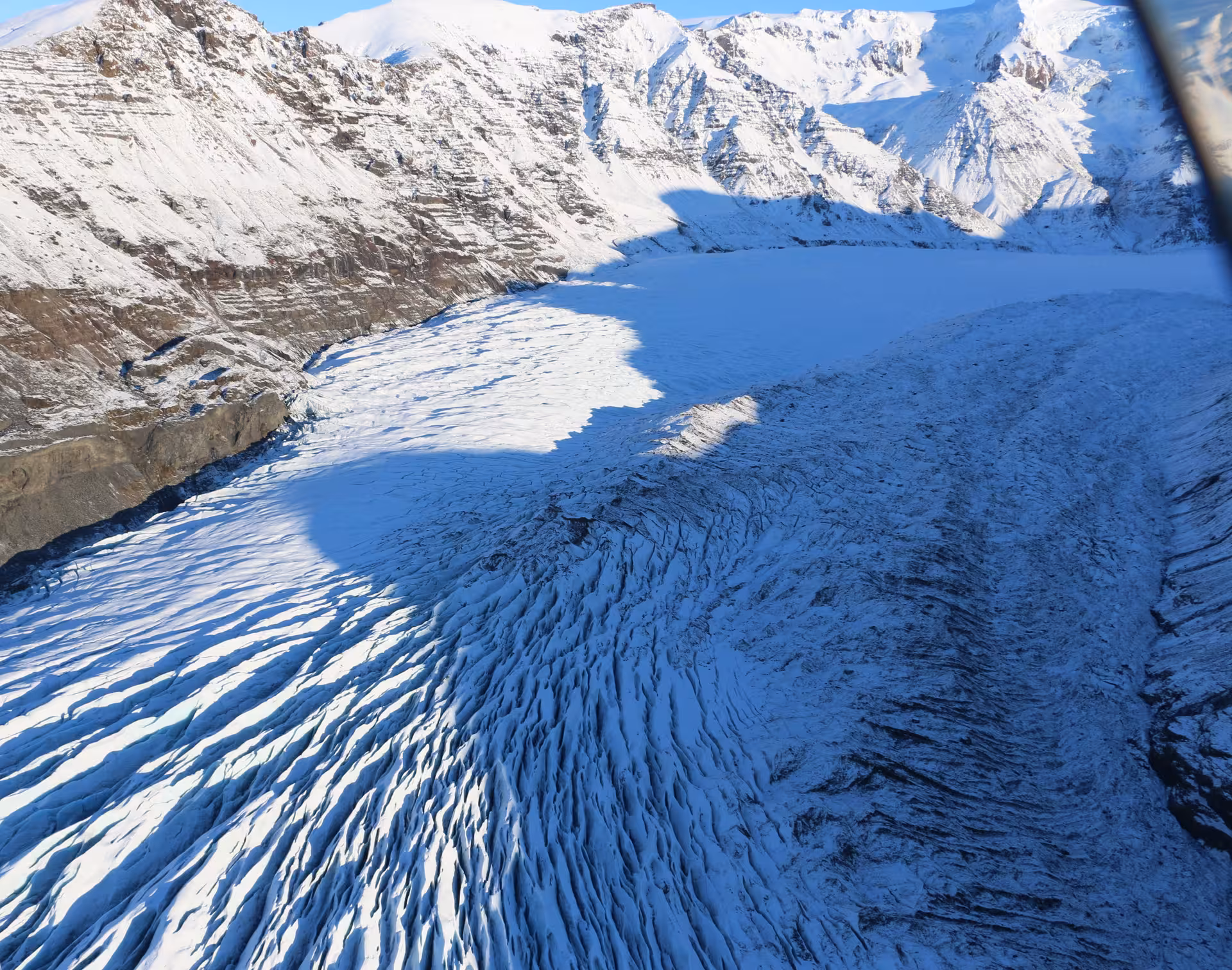 Aerial view of a heavily crevassed glacier flowing between snow-covered mountains in Iceland