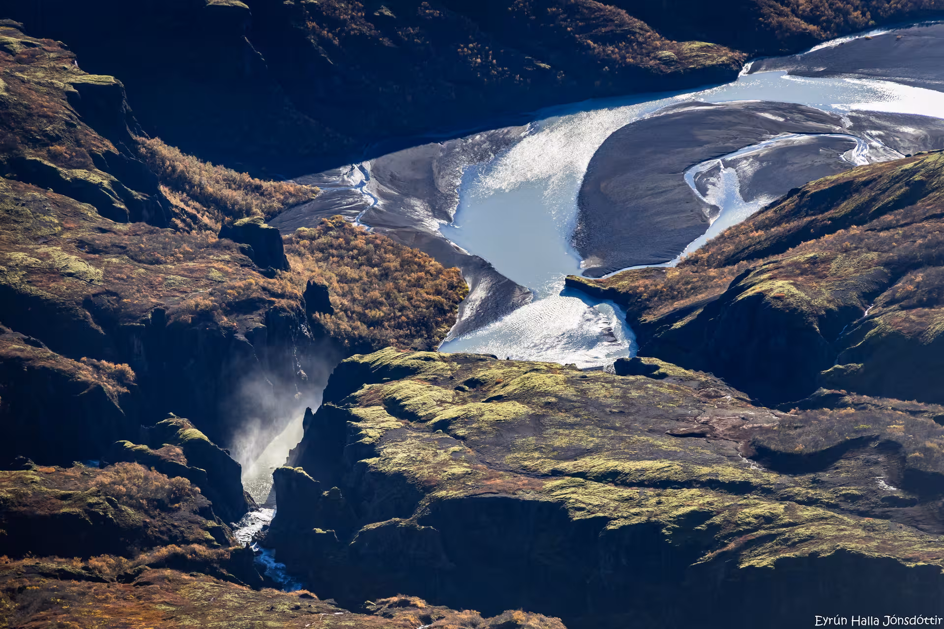 Aerial view of Icelandic glacier with glacial lake, mossy lava fields, and waterfall below
