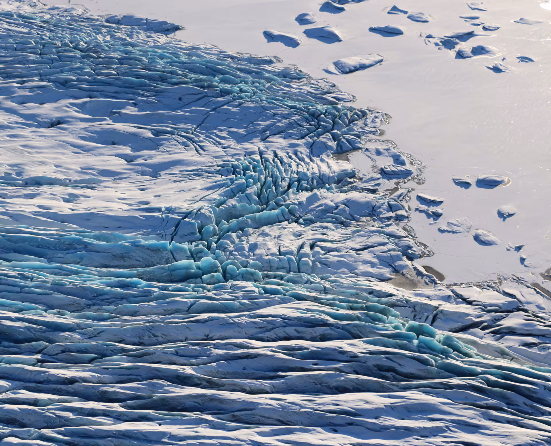 Aerial view of a glaciers jagged blue ice formations and crevasses meeting a frozen lake in Iceland