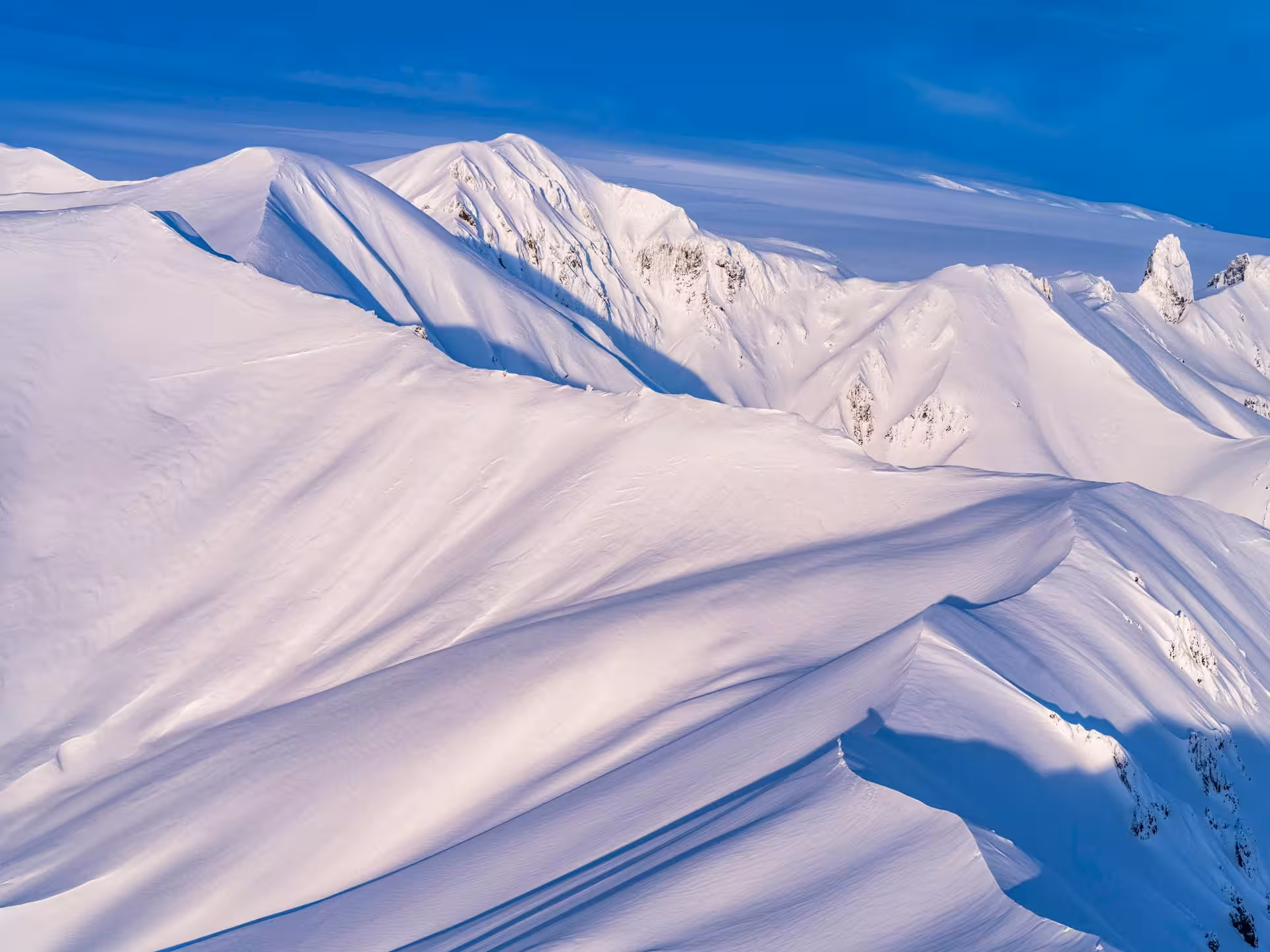 Snow-covered glacier mountain ridges under blue sky in Iceland aerial view