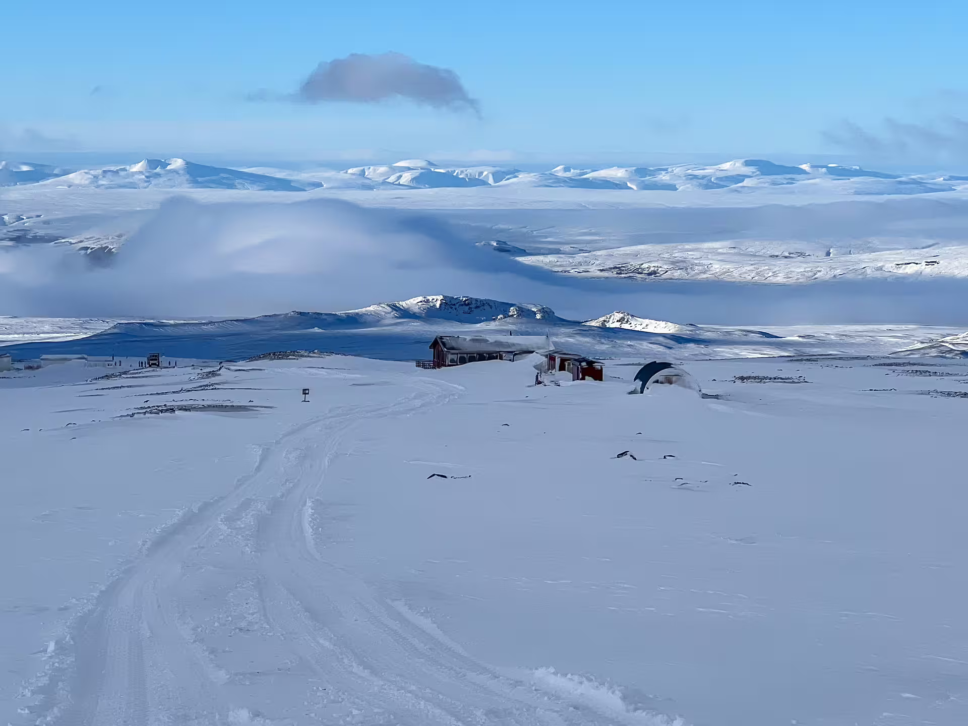Snow-covered highland plateau with red mountain hut, misty glacier landscape and volcanic peaks in background