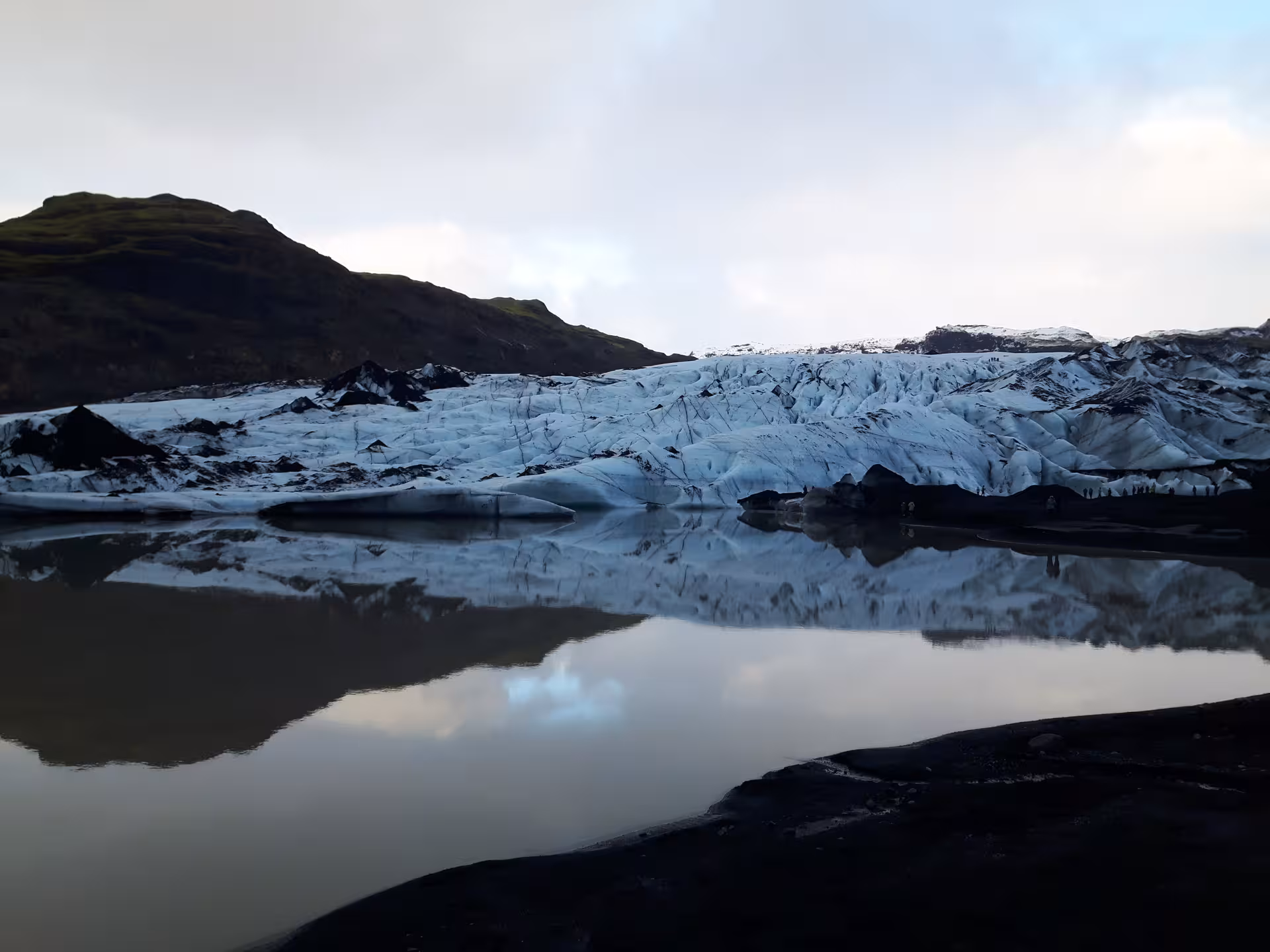 Glacier face with black volcanic rock and calm reflective lagoon at Iceland glacier hike tour