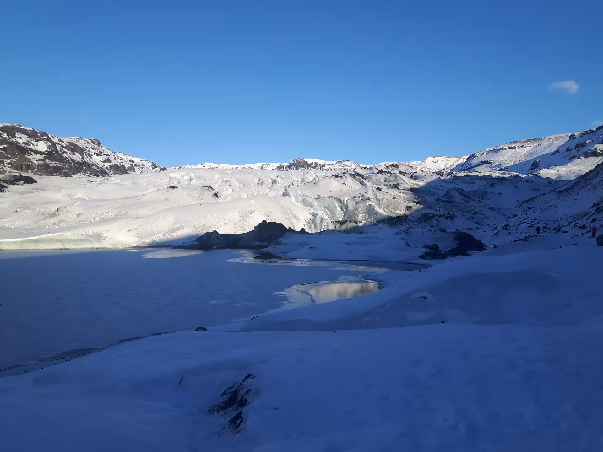 Vast glacier landscape with snow-covered ice field and small meltwater pool under clear blue sky in Iceland