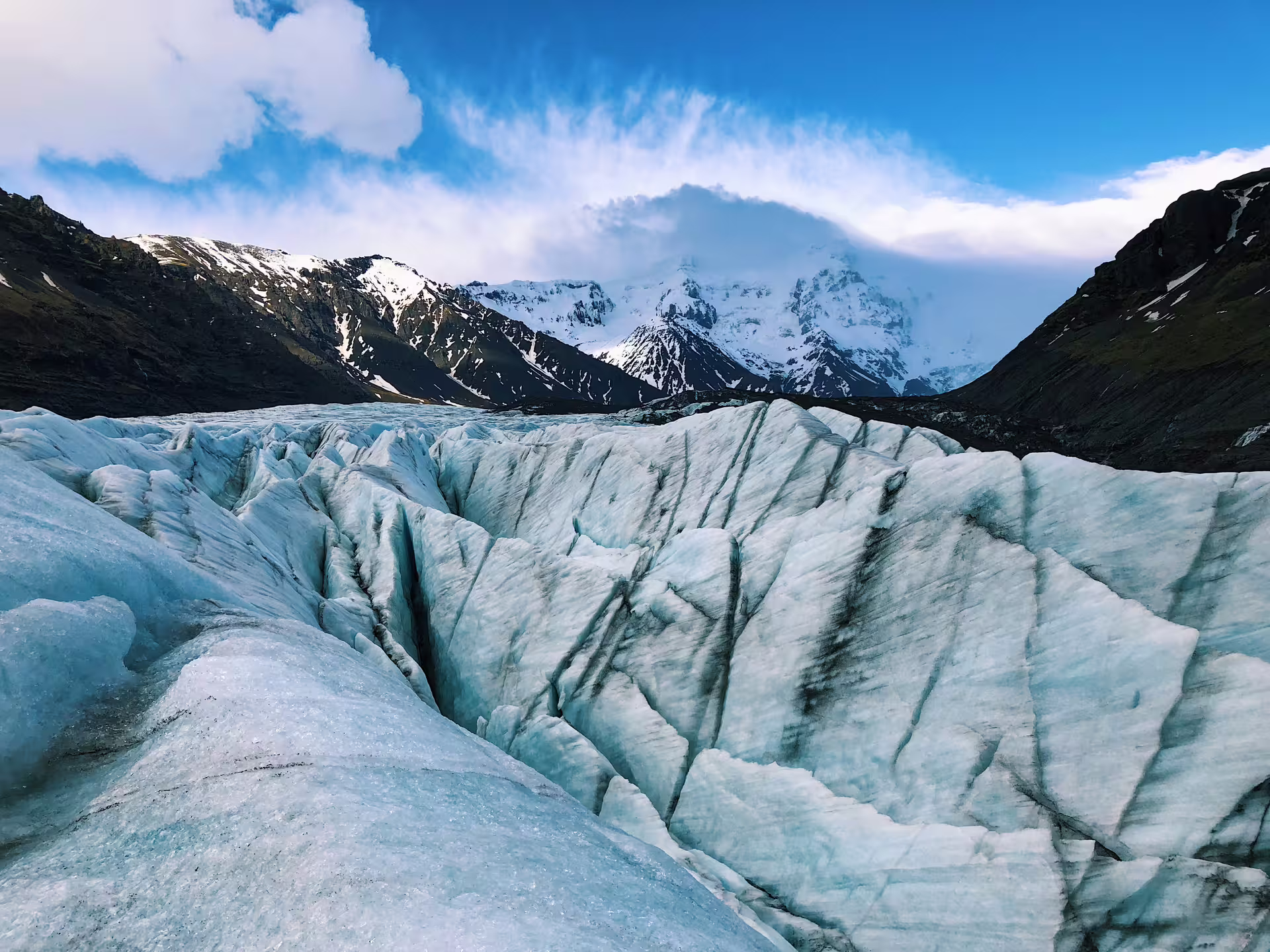 Blue glacial ice formations with crevasses and snow-capped mountains in Iceland's South Coast