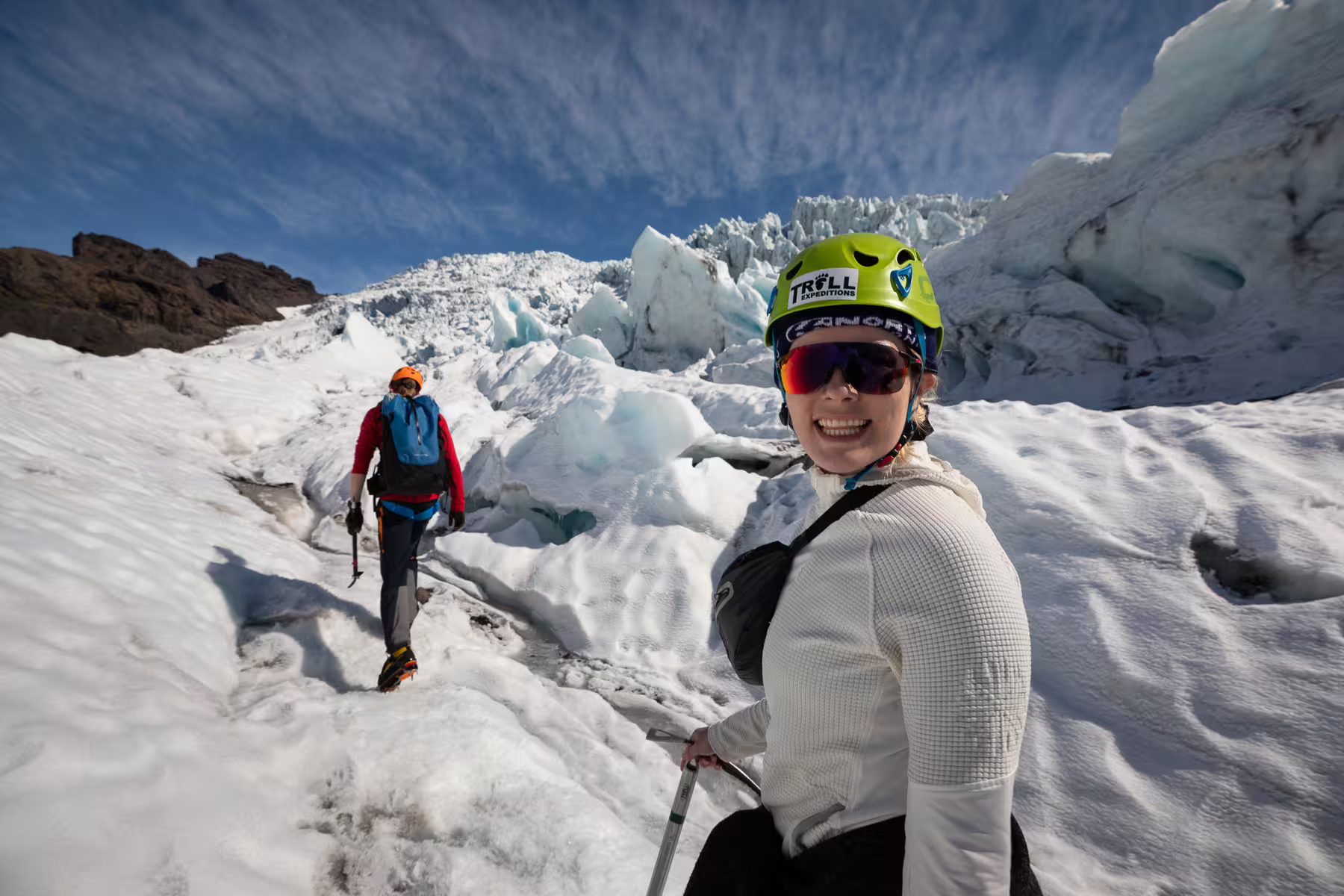 Smiling hiker with Troll Expeditions helmet on Iceland glacier with ice formations and blue sky