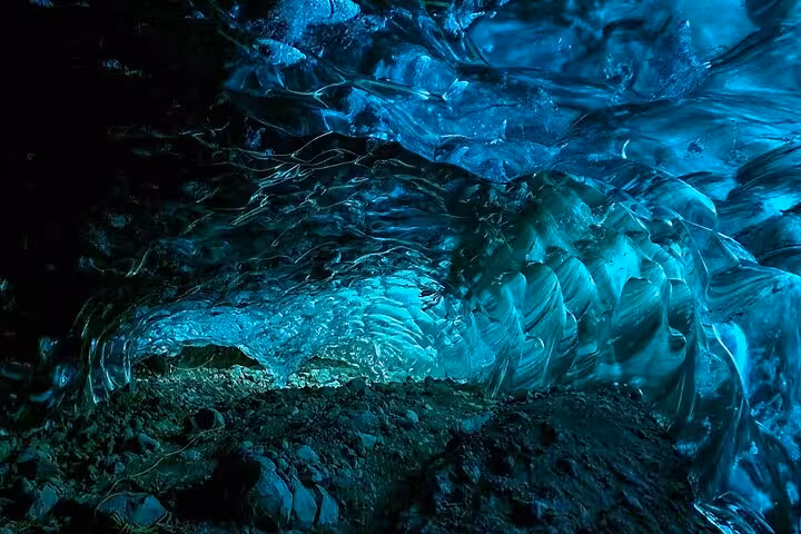 Glowing turquoise blue ice cave tunnel inside an Icelandic glacier with rocky floor