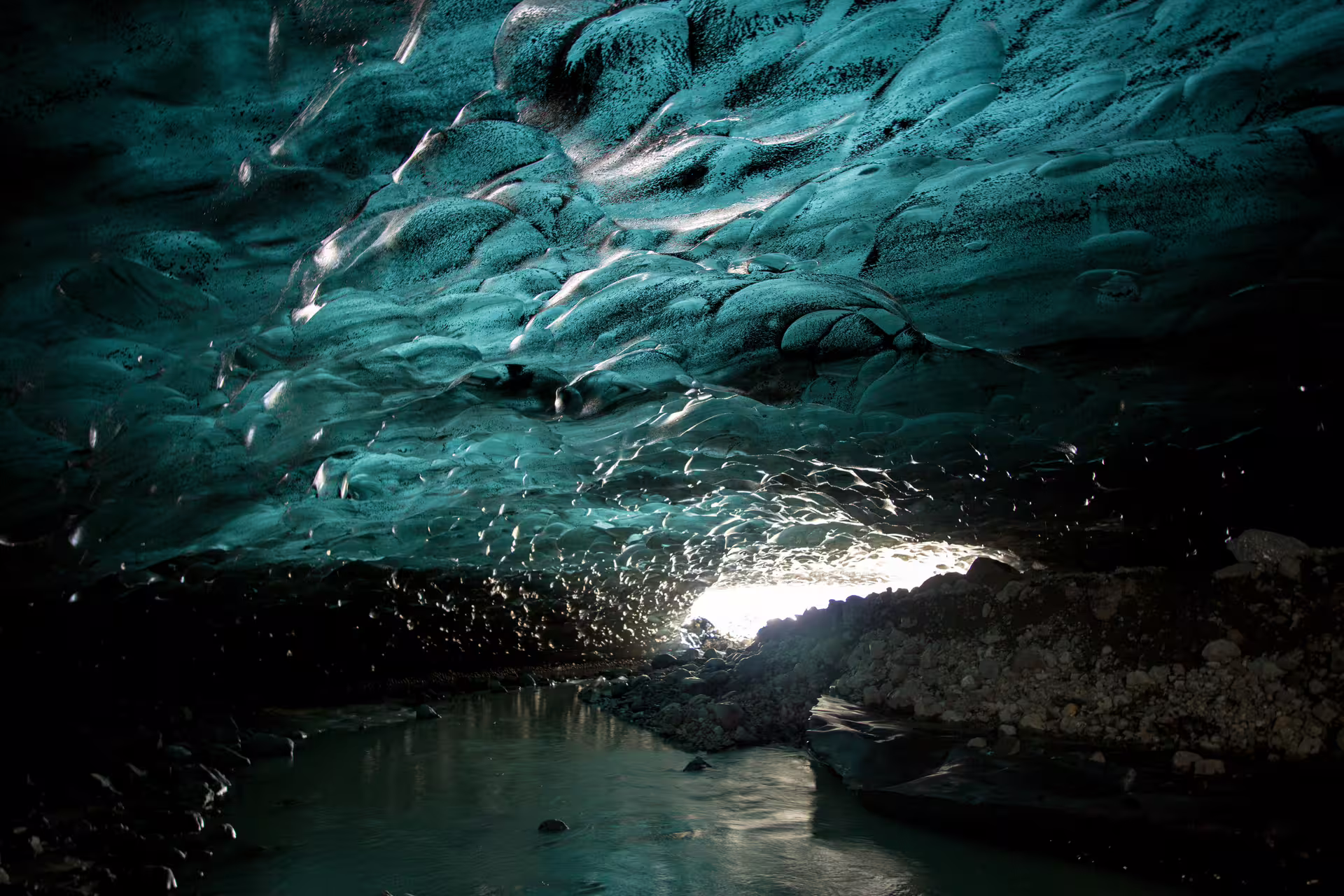 Glowing teal ice cave tunnel with stream in Iceland glacier