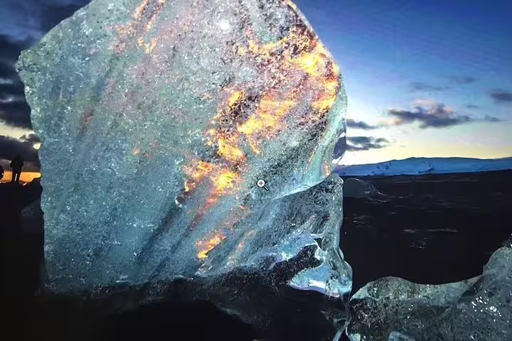 Large translucent ice chunk glowing with sunset light on Iceland's black sand beach