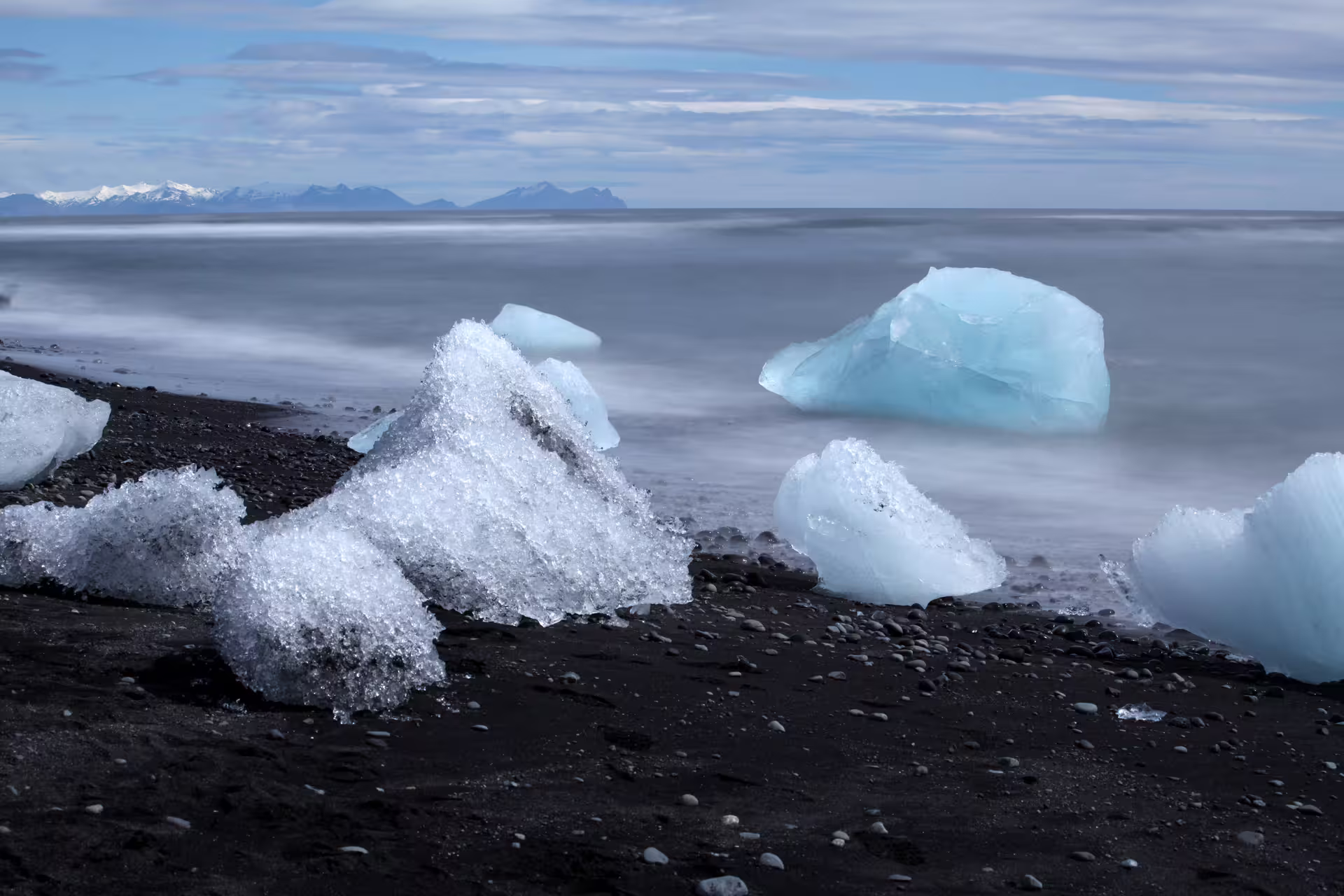 Ice chunks on black sand beach with glacial blue icebergs and misty ocean in Iceland