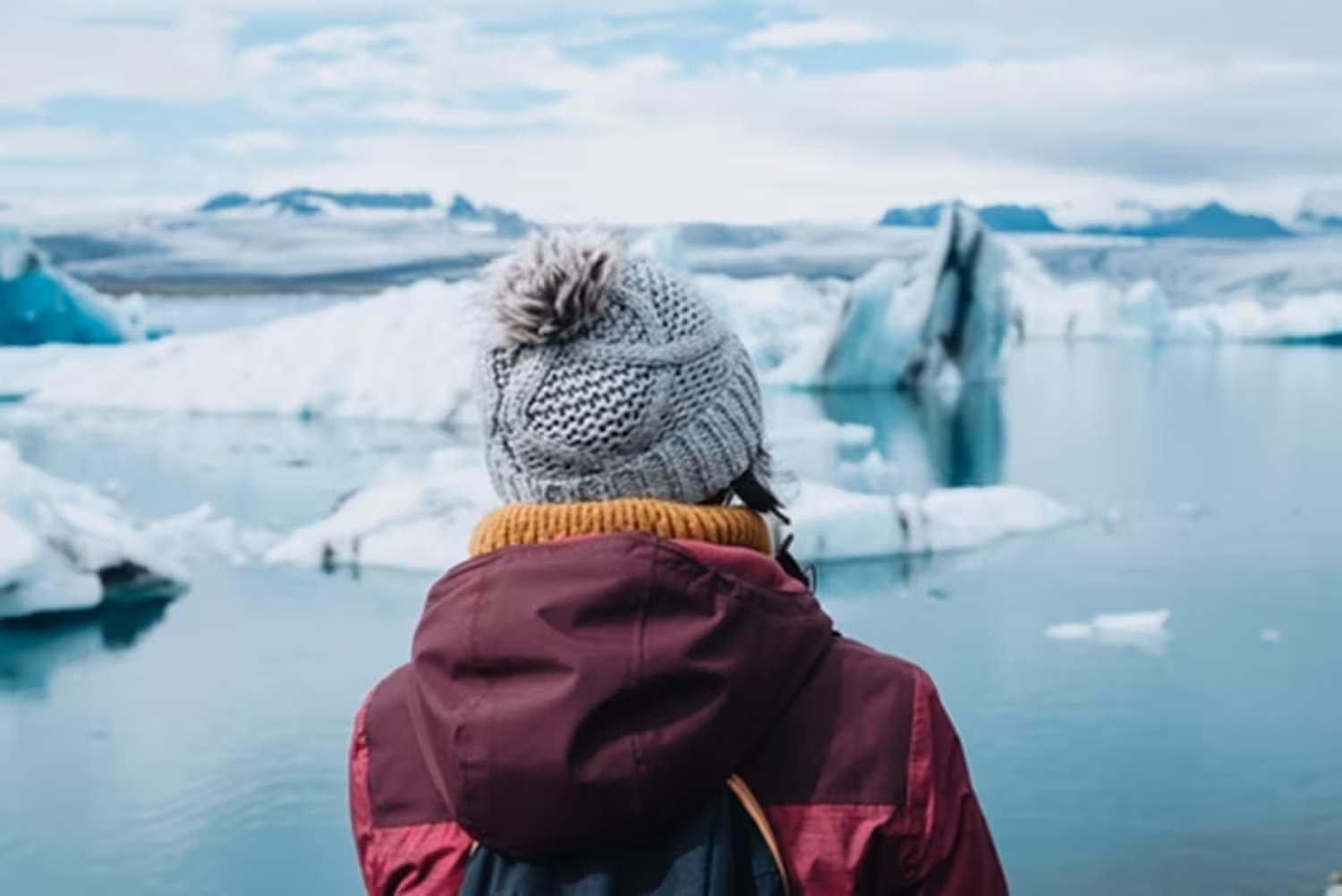Traveler in winter jacket and knit hat gazing at icebergs floating in Glacier Lagoon, Iceland