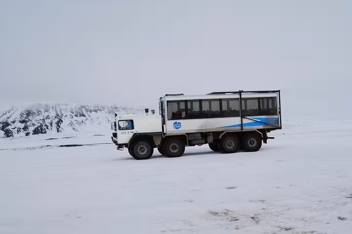 Large white monster truck glacier vehicle driving across snowy Iceland landscape with mountains in background