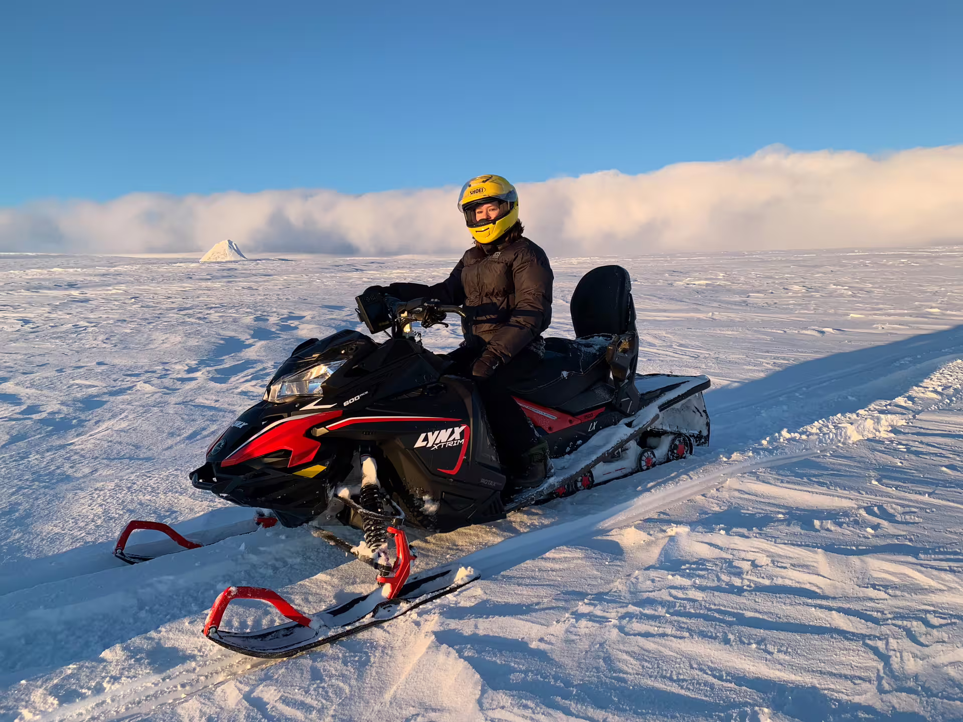 Rider in yellow helmet on Lynx Xtrim snowmobile on Iceland glacier snowfield under blue sky