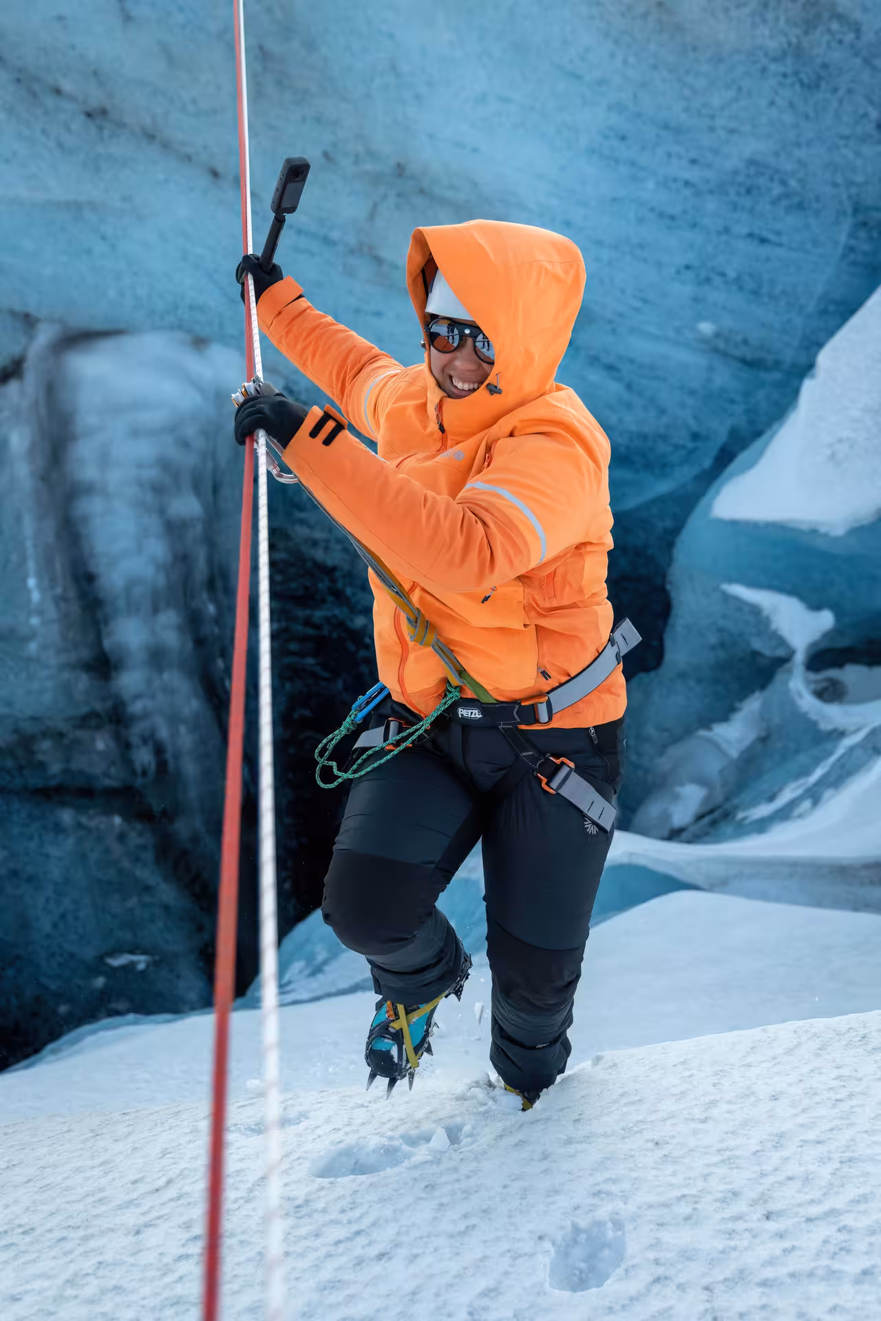 Smiling guide in orange jacket with harness and crampons on an Iceland glacier zip line winter adventure tour