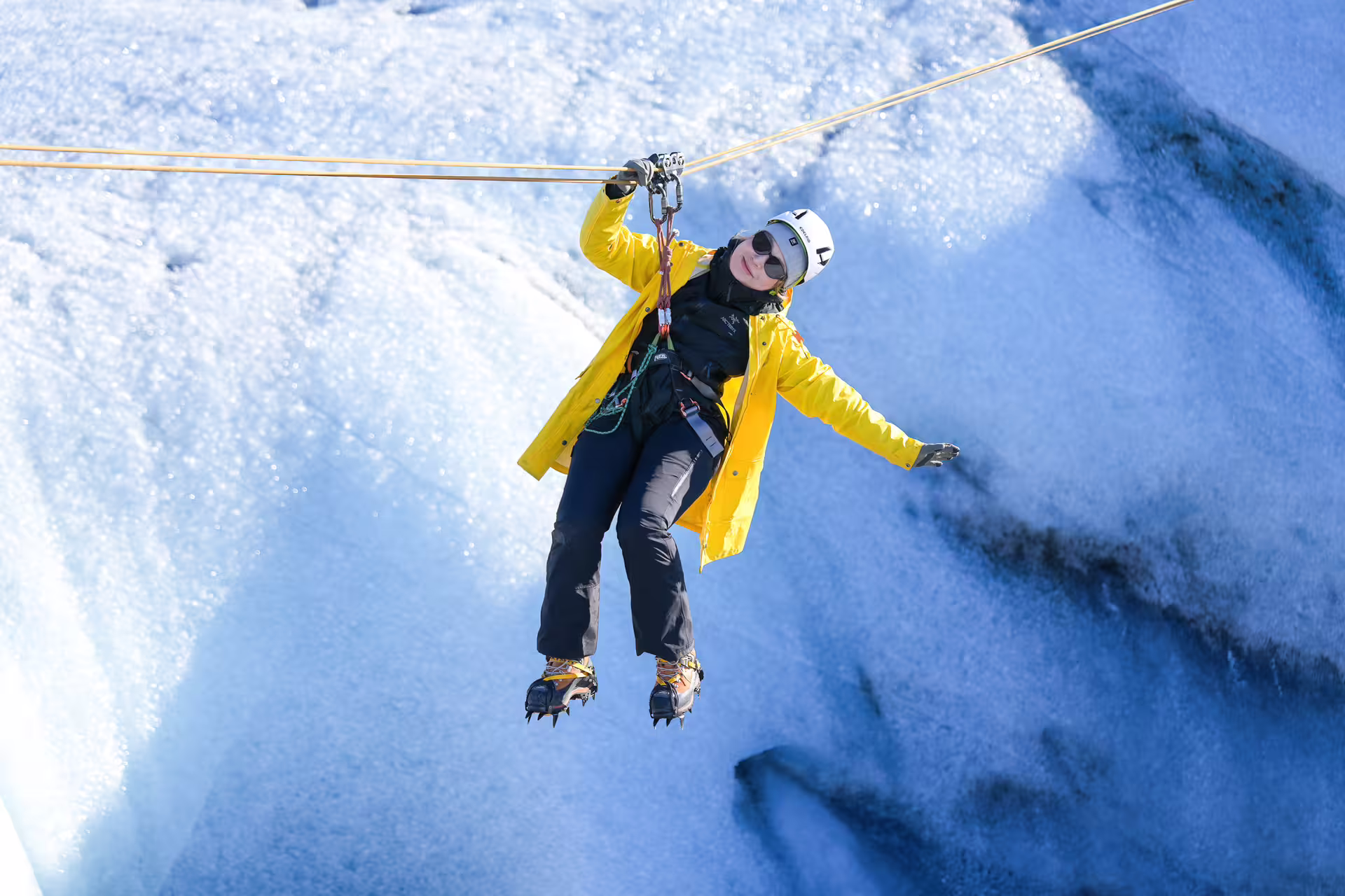 Thrilling glacier zip-line adventure in Iceland with a smiling traveler in yellow jacket and crampons on Grand Tour