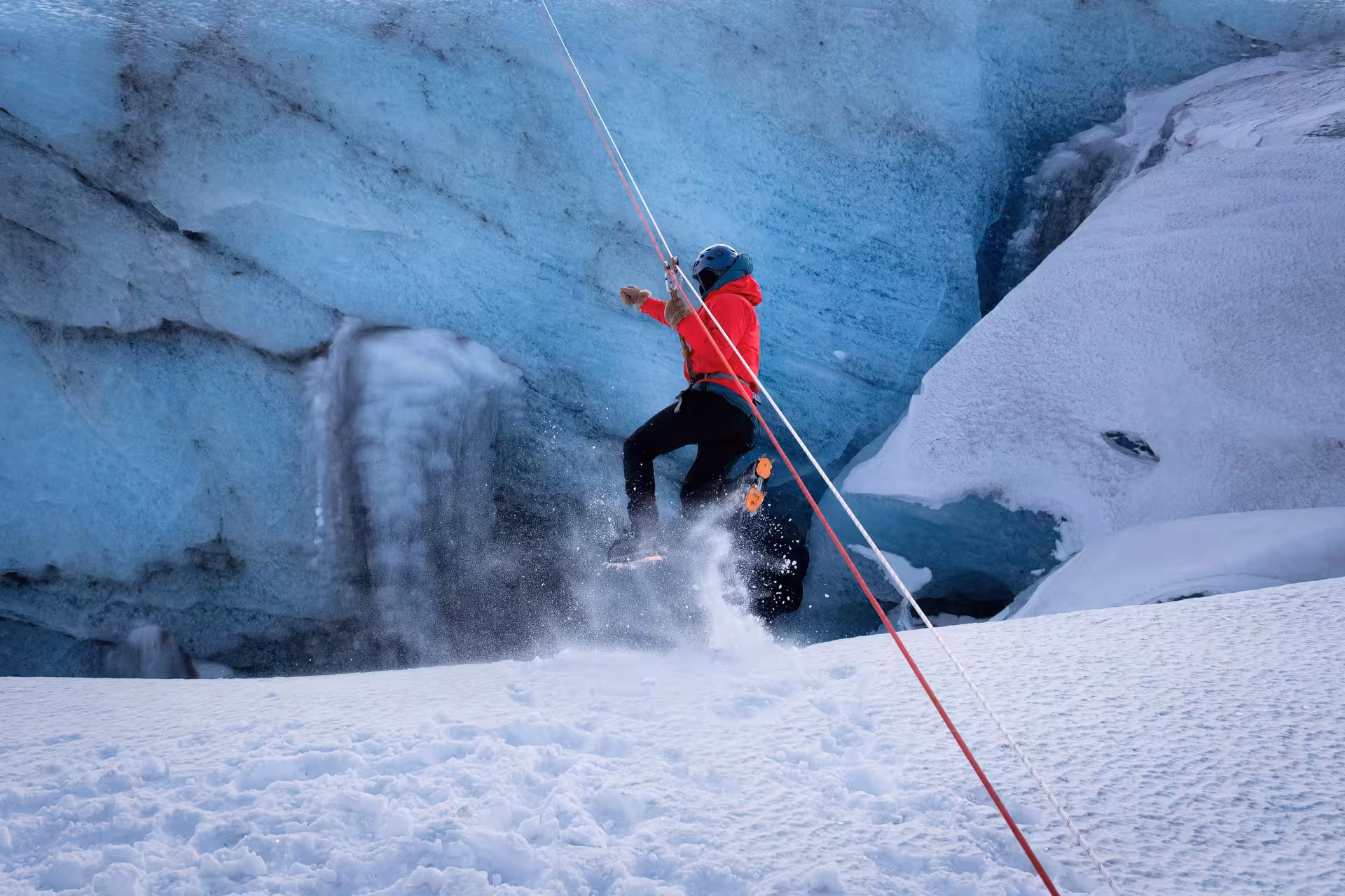 Guided glacier zip line adventure in Iceland with participant in red jacket rappelling snowy ice wall