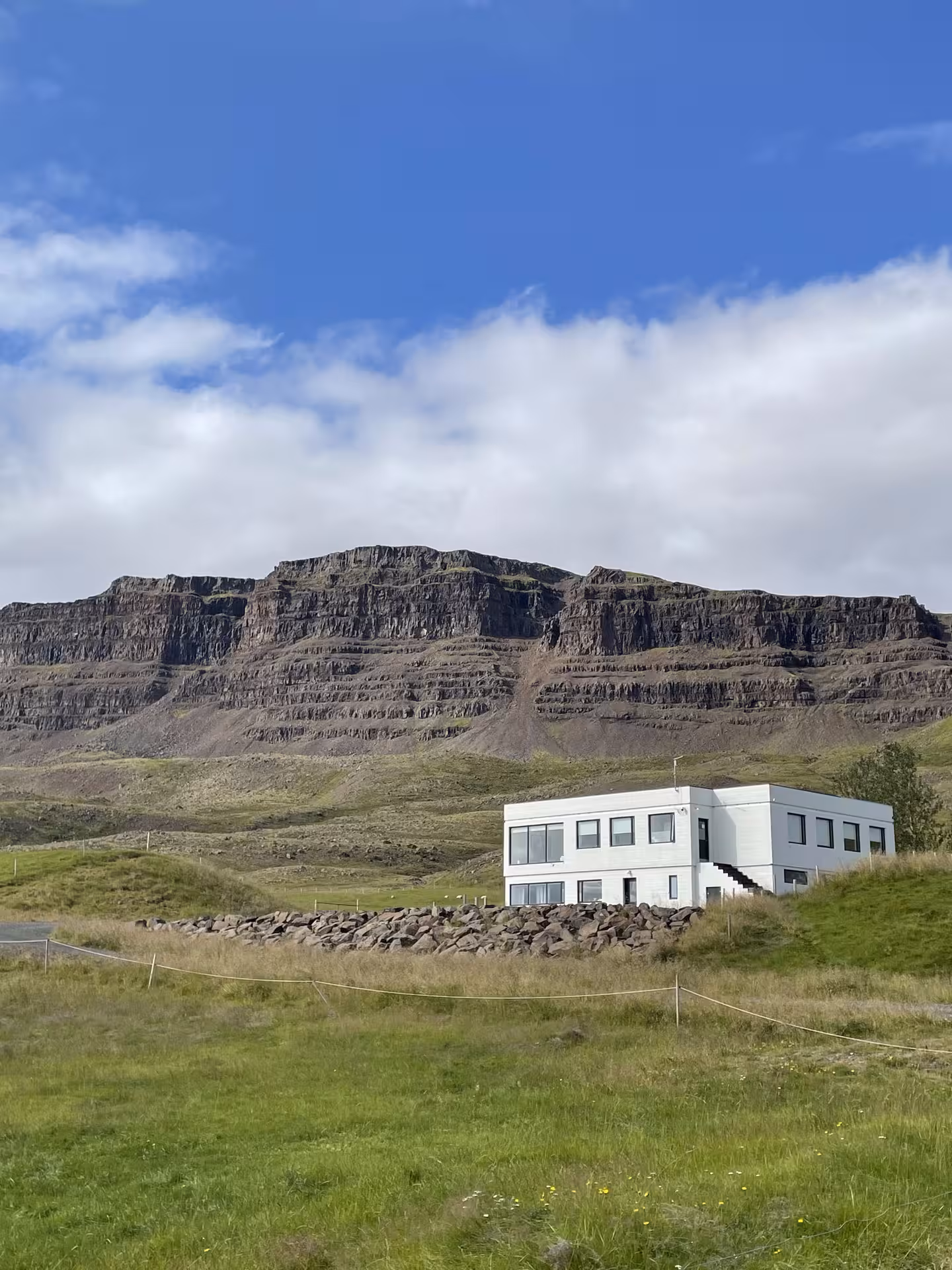 White two-story farmhouse against dramatic layered basalt cliffs on Iceland's Golden Circle route