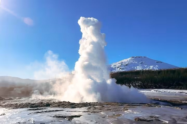 Geyser erupting with steam and snow-capped mountain in Iceland's Golden Circle
