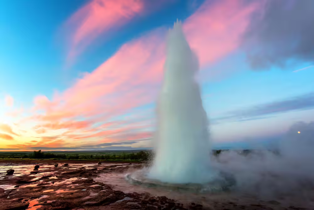Strokkur geyser erupting at sunset with pink clouds and steam in Iceland's Golden Circle
