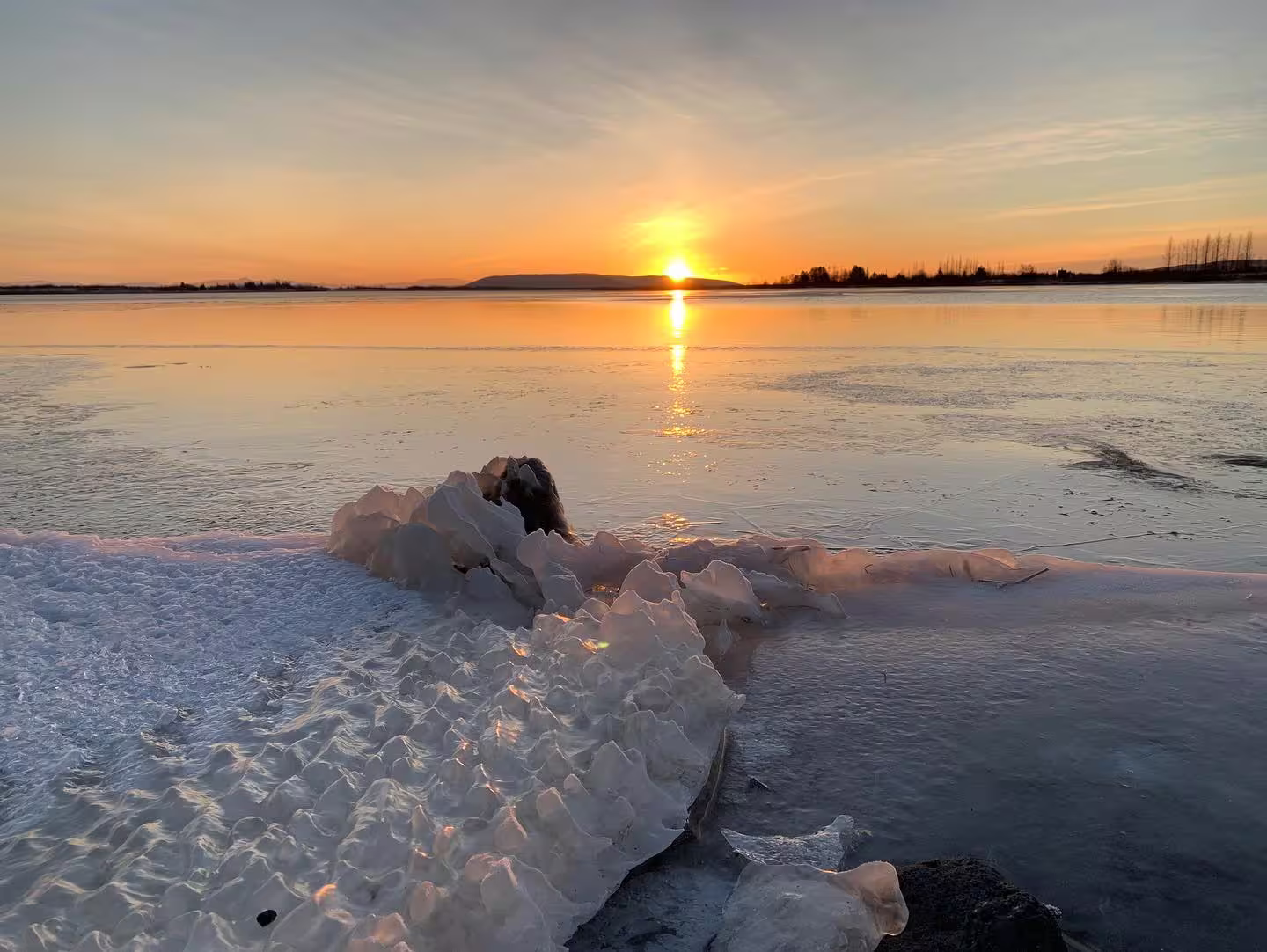 Icy shoreline with textured ice formations at golden sunset over a frozen Icelandic lake