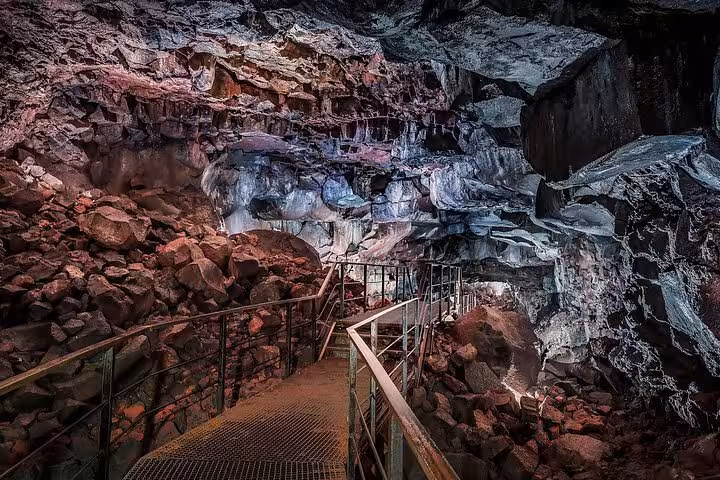 Metal walkway through illuminated lava cave tunnel with red volcanic rocks in Iceland