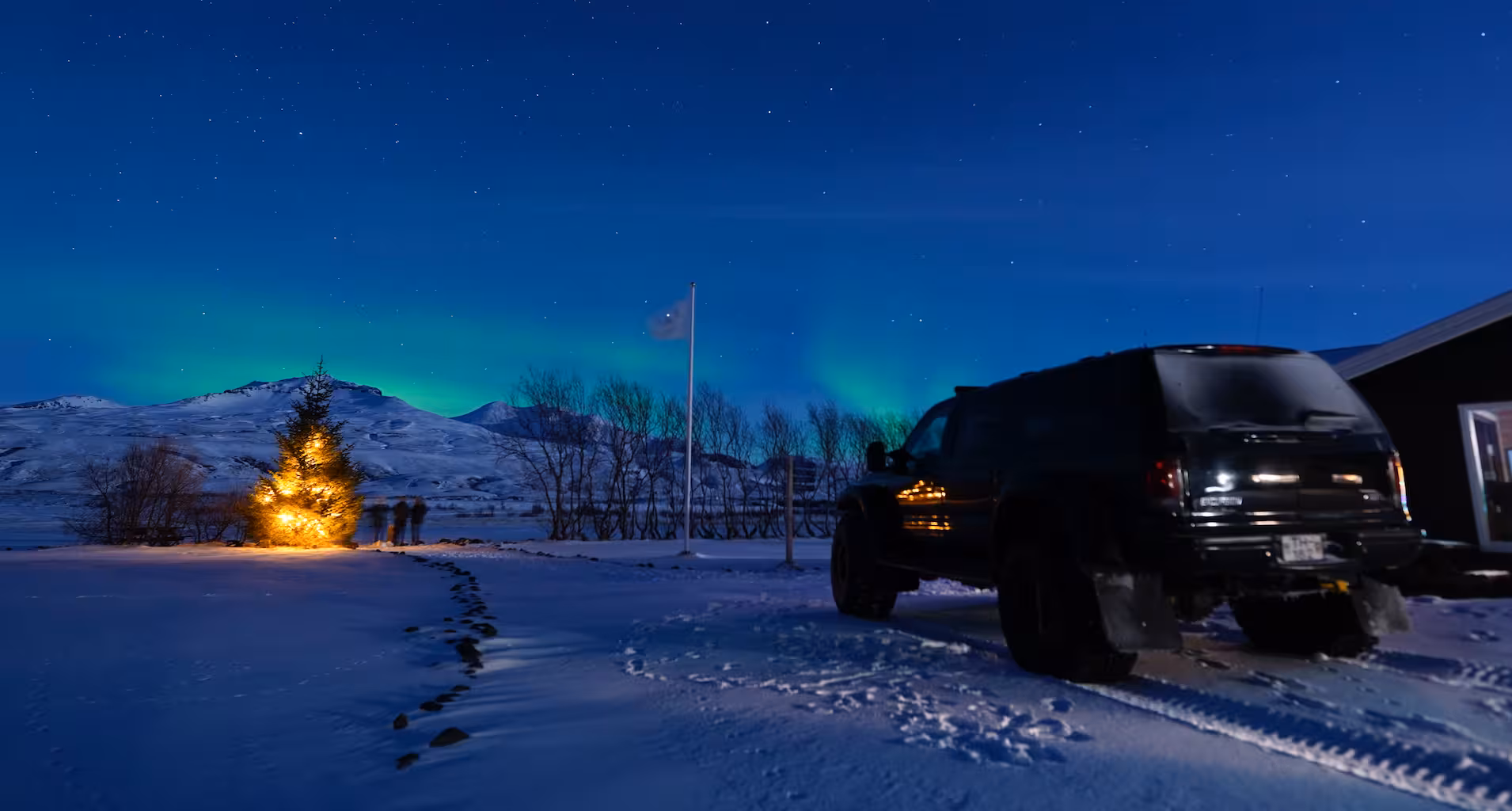 Black SUV parked in snowy Iceland landscape with northern lights glowing over mountains at night