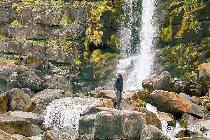 Traveler standing on mossy rocks beside a cascading waterfall in Iceland